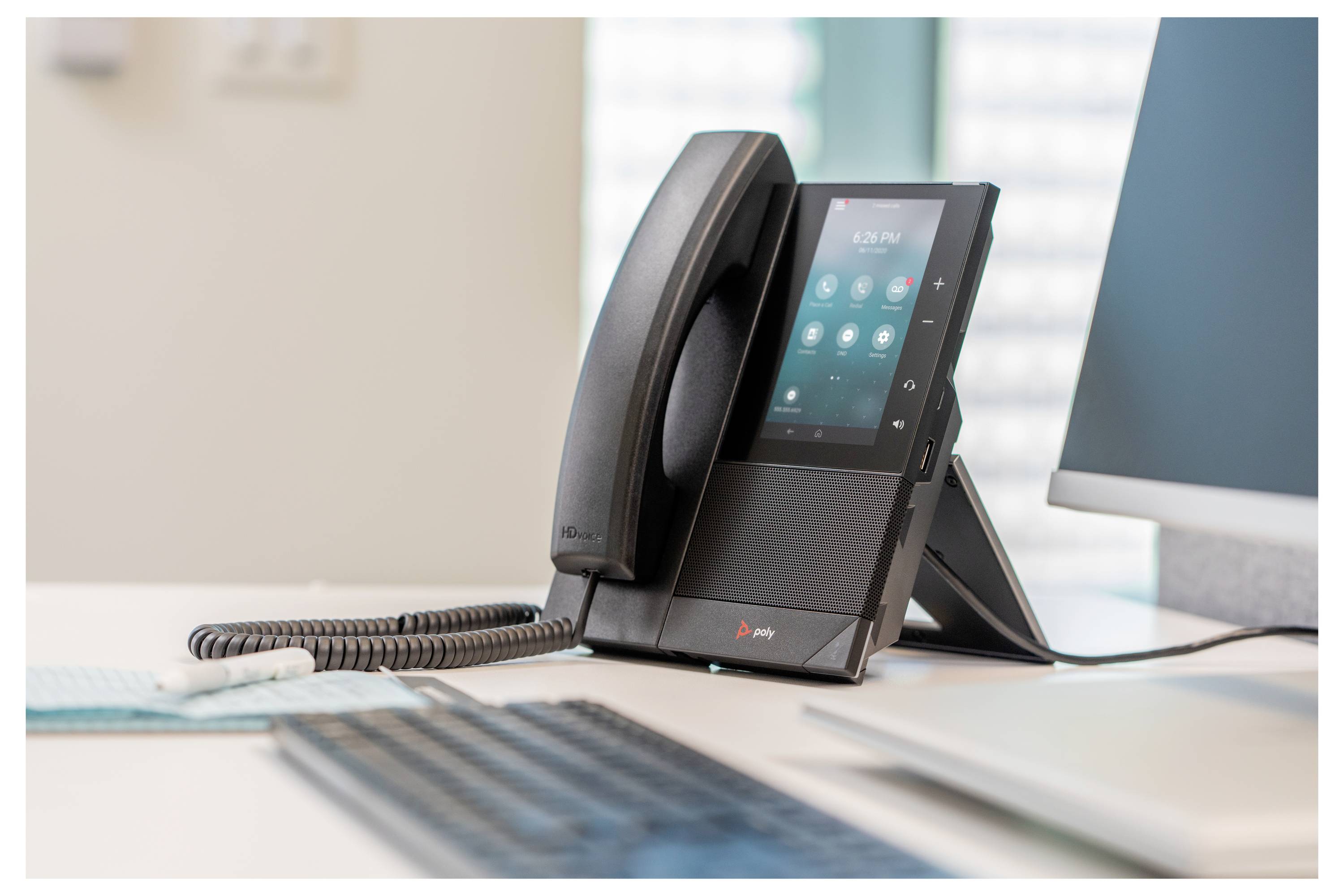 Ein Büro-Schreibtischtelefon mit Touchscreen-Display und Hörer auf seinem Ständer, mit Spiralkabel im Vordergrund.