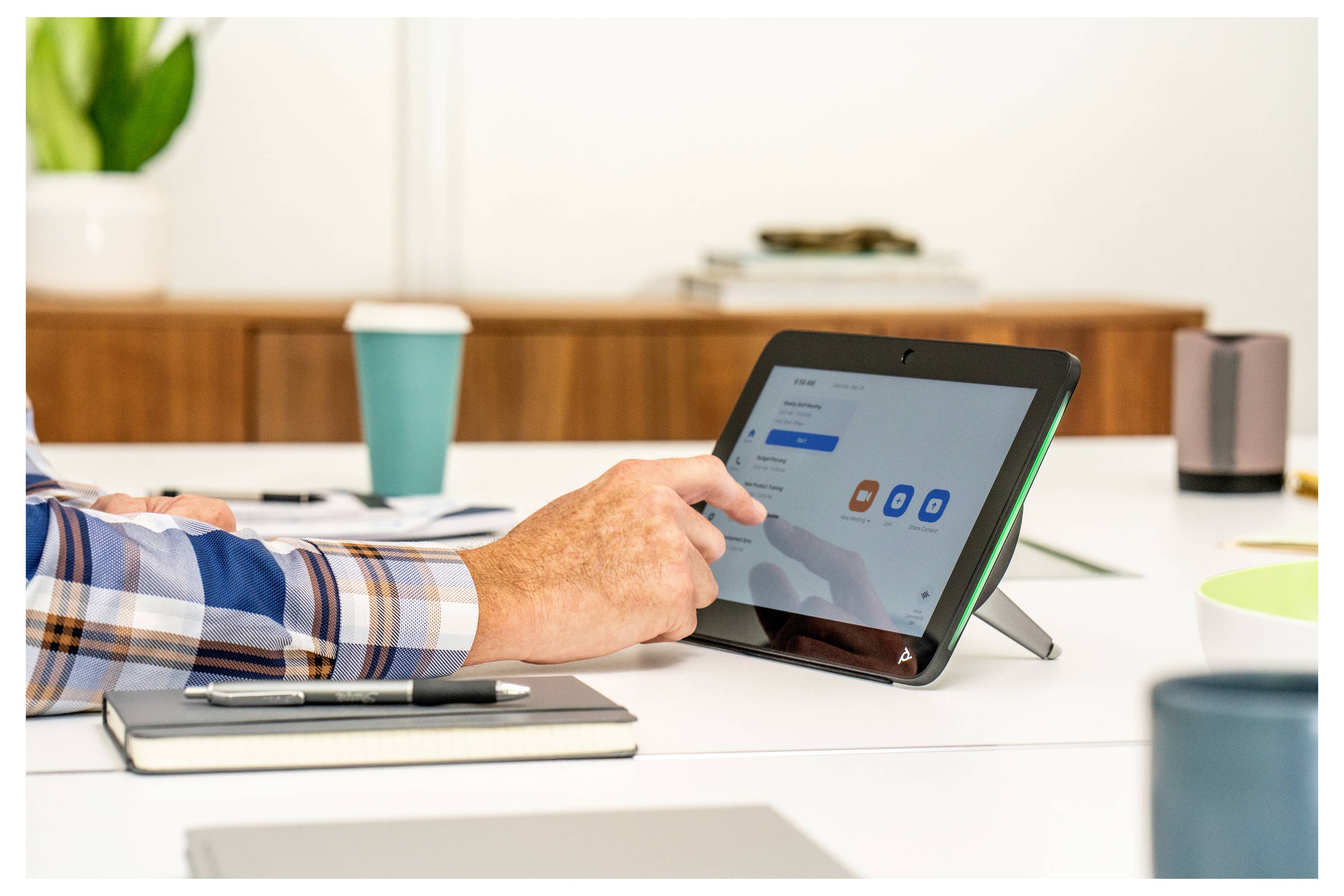Eine Person nutzt ein Tablet auf einem Schreibtisch in einem Büro, tippt auf einen Bildschirm mit App-Symbolen neben einem Notizbuch, einem Stift und einer Kaffeetasse.