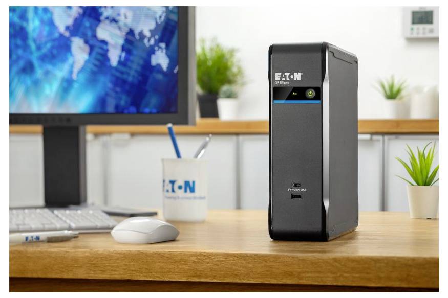 Schwarze Eaton-Batterie-Backup-Einheit auf einem Schreibtisch in einem modernen Büro neben einer Tastatur und einer Maus, mit einem Computermonitor im Hintergrund.