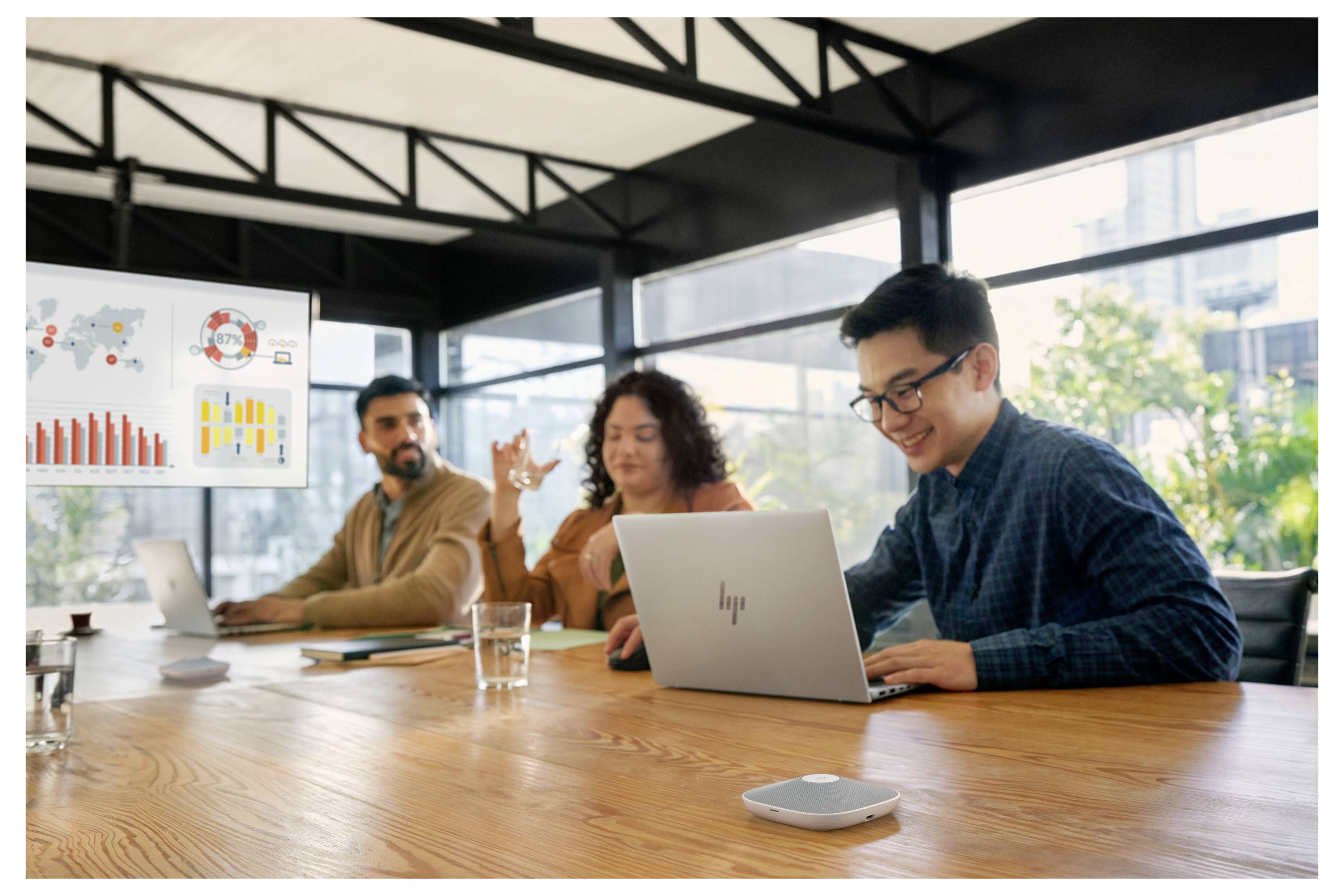 Teammeeting in einem modernen Büro: Drei Kollegen überprüfen Analysen auf einer Wandanzeige, während einer an einem Laptop am Konferenztisch arbeitet.