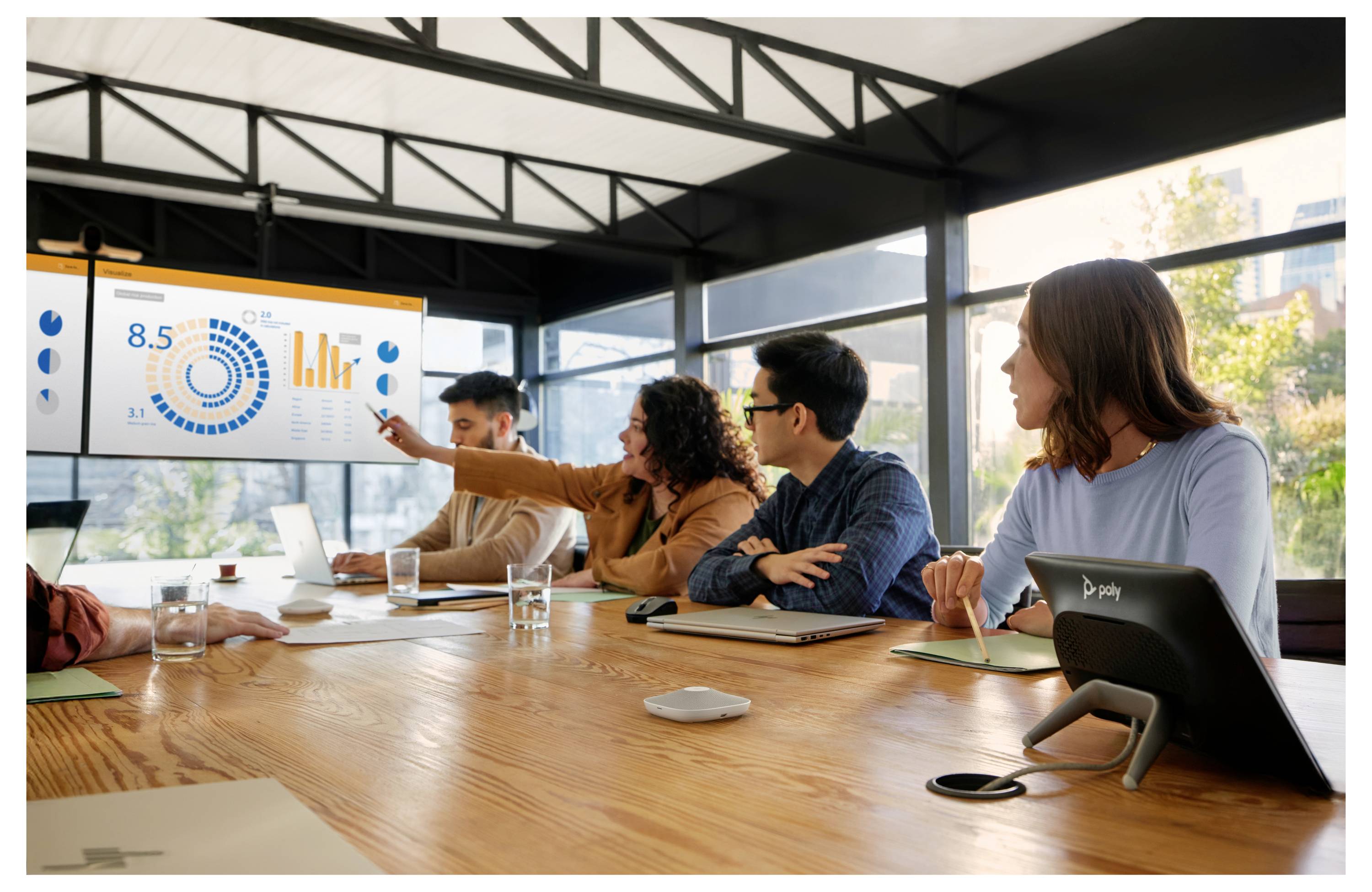 Ein Team sitzt um einen Konferenztisch herum, während eine Person Analysen auf einem großen Wanddisplay präsentiert.