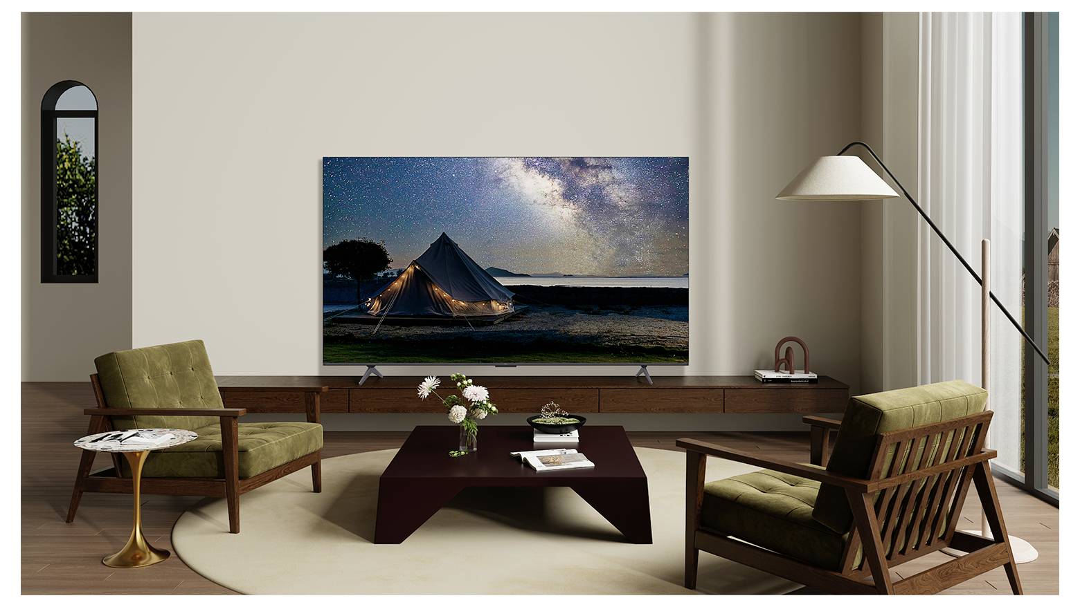 Ein modernes Wohnzimmer mit zwei grünen Sesseln, einem braunen Couchtisch und einem Flachbildfernseher, der eine Sternennacht mit einem beleuchteten Zelt zeigt.