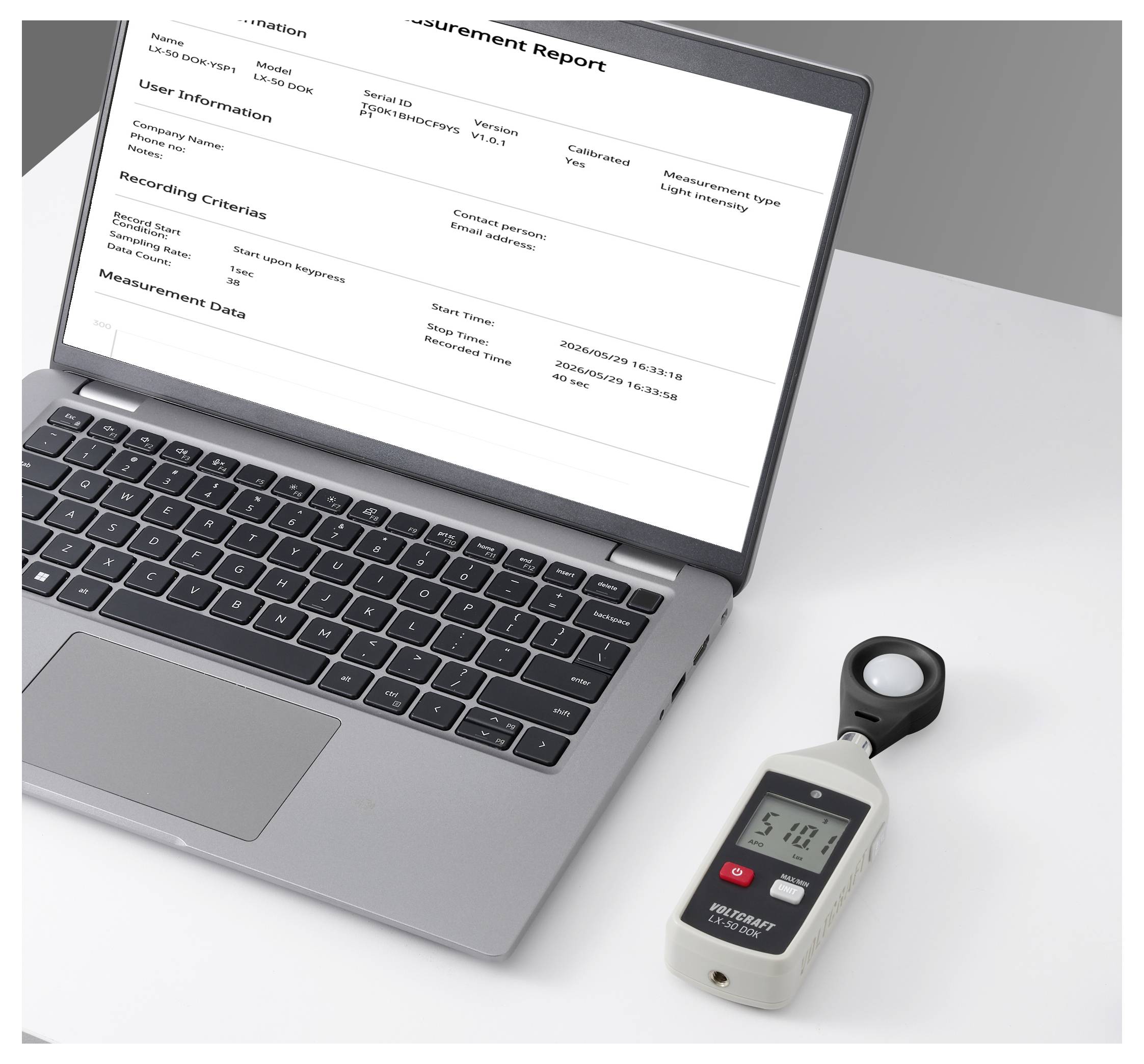Laptop, das einen Messbericht auf einem weißen Schreibtisch neben einem tragbaren Lichtmessgerät/Sensor anzeigt.
