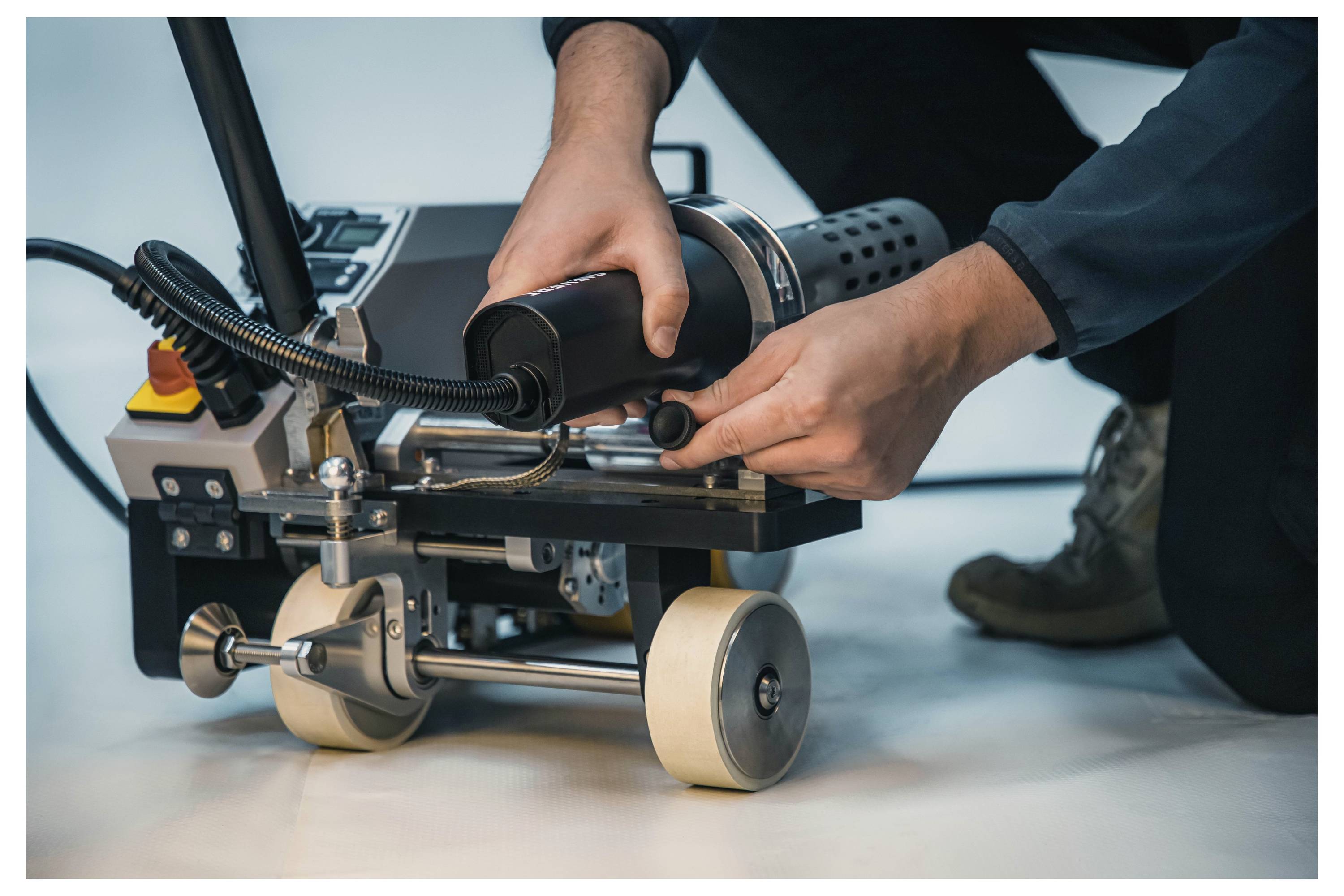 Eine Person bedient eine kompakte Industriemaschine auf Rädern und stellt mit beiden Händen die Steuerelemente ein, was auf Wartungs- oder Einrichtungsarbeiten hindeutet.
