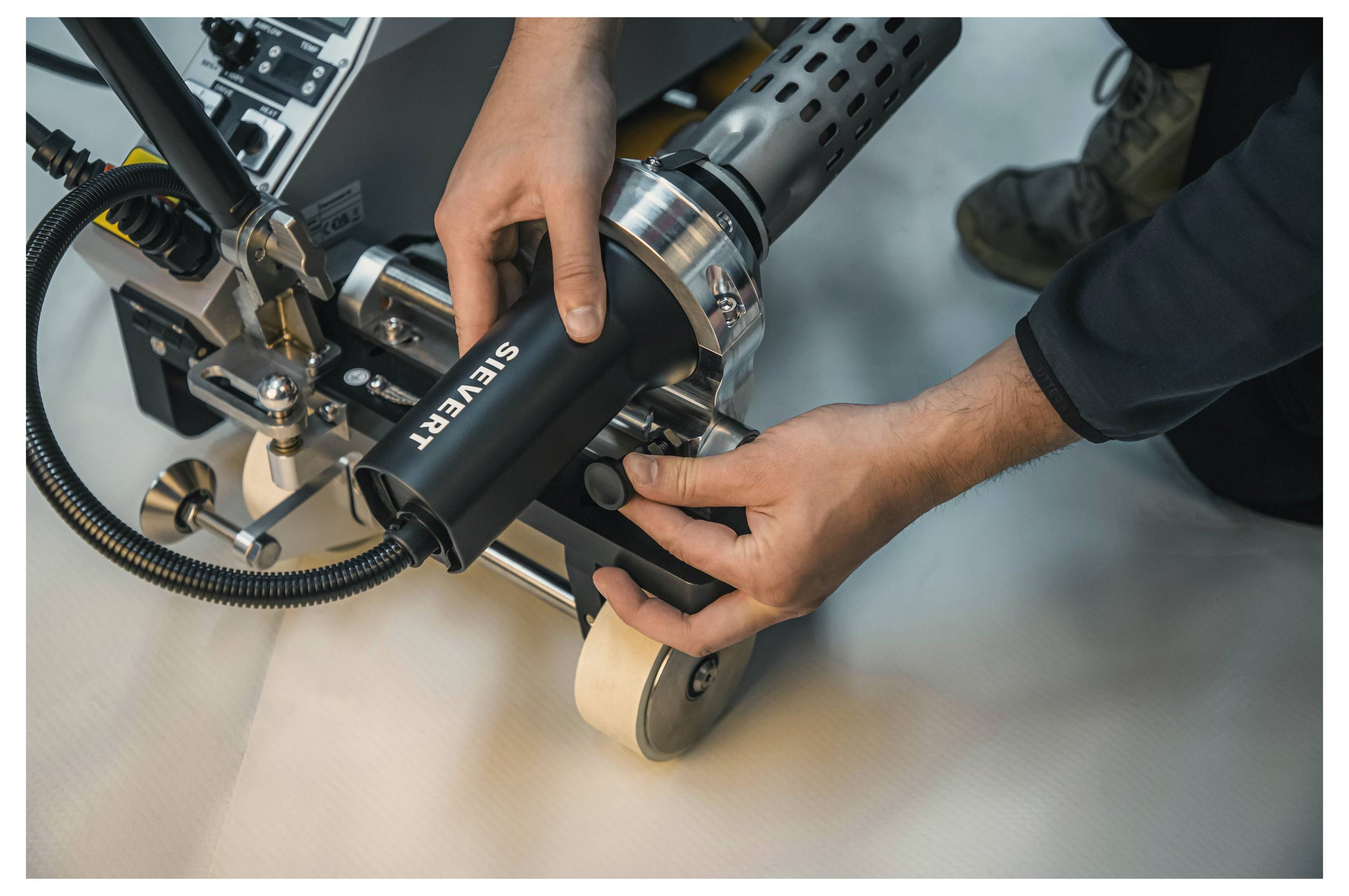 Hände, die eine Maschine zum Heißluftschweißen von Kunststofffolien einstellen, wobei präzise Gerätebedienung und technische Kompetenz hervorgehoben werden.