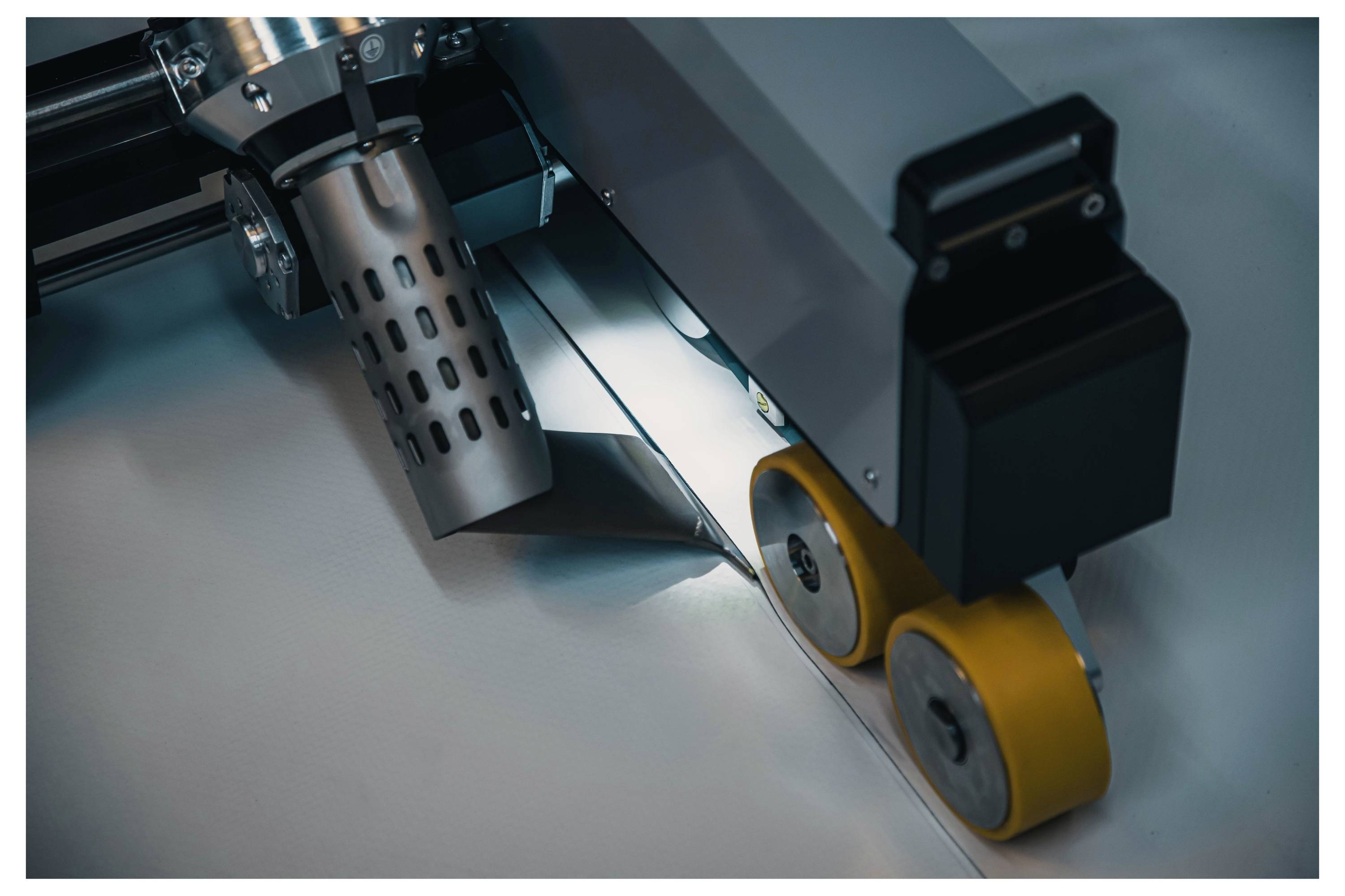 Eine Maschine mit gelben Rädern wendet Wärme an, um eine Naht auf einem grauen Material zu verschweißen, wahrscheinlich für industrielle oder Fertigungszwecke verwendet.