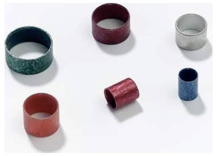 Sechs zylindrische Metallringe in verschiedenen Farben, darunter rot, blau, grün und silber, sind auf einem weißen Hintergrund verstreut.