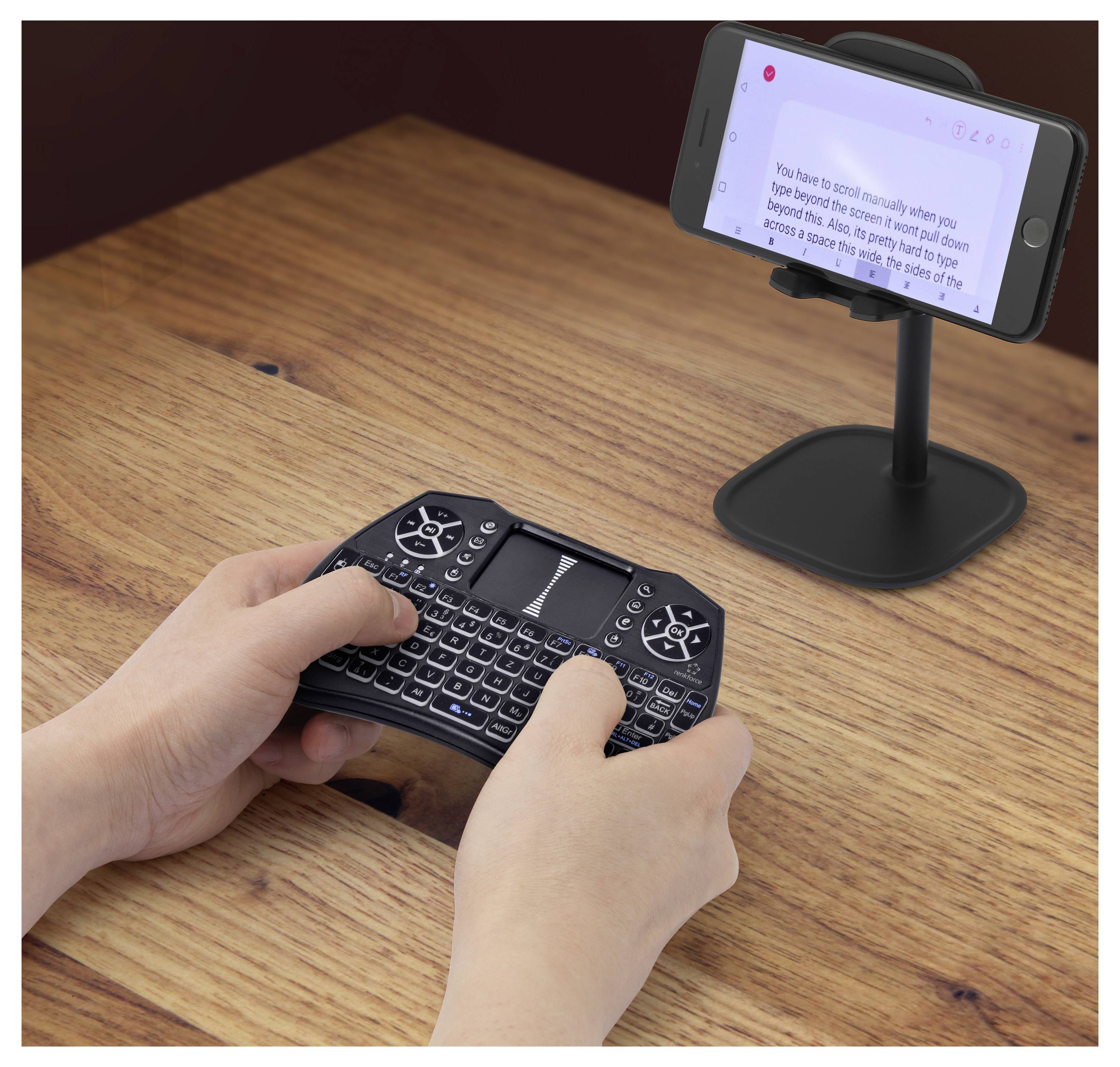Hände, die einen kompakten kabellosen Tastatur-Spielecontroller verwenden, während ein Smartphone auf einem Ständer einen Bildschirm anzeigt, was auf die Steuerung von Mobilspielen hindeutet.