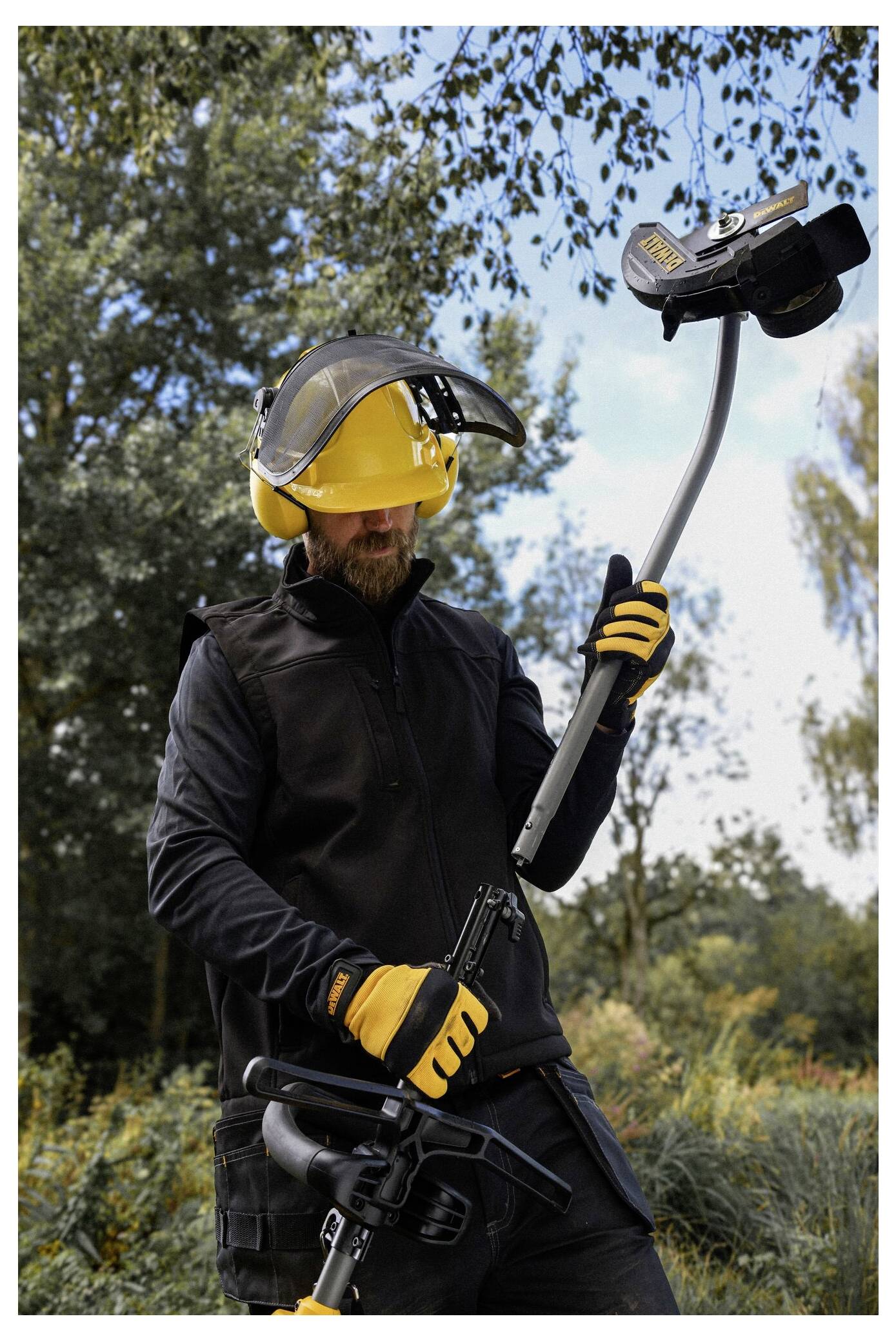 Eine Person, die Schutzausrüstung trägt, einschließlich eines Helms, eines Schildes und von Handschuhen, hält und überprüft ein Gerät im Freien in einem bewaldeten Gebiet.