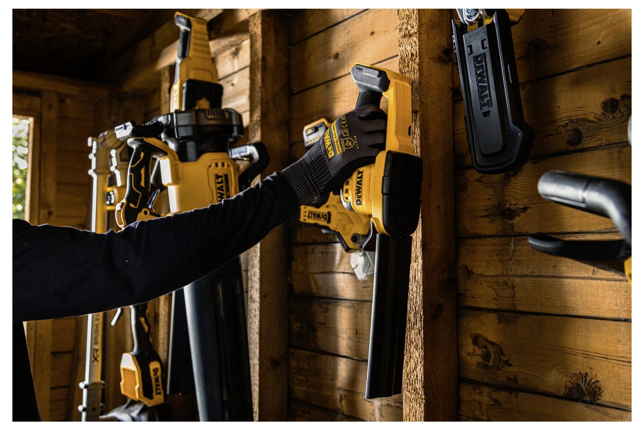 Eine Person in einem Schuppen organisiert gelbe und schwarze Elektrowerkzeuge an einer Holzwand. Verschiedene Sägen und Bohrer hängen ordentlich an ihren Plätzen.
