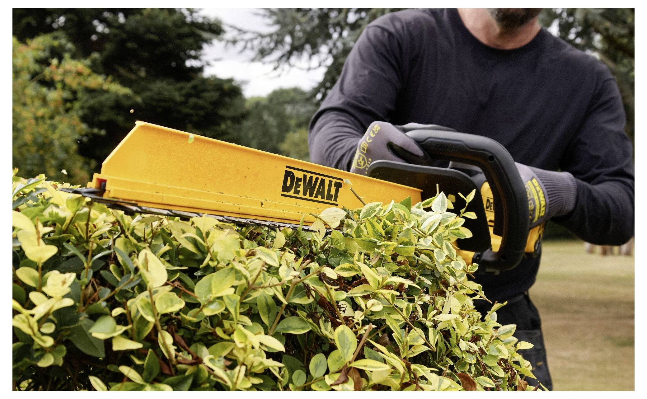 Eine Person trimmt eine Hecke mit einer DeWalt-Heckenschere in einer Gartenumgebung.