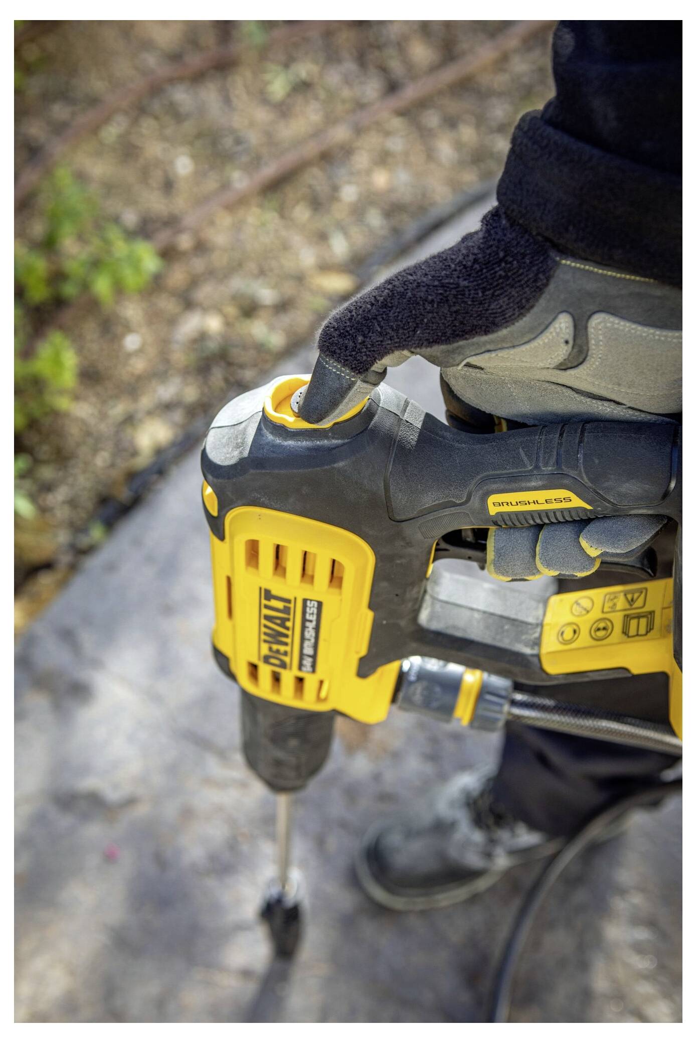 Eine Person mit Handschuhen bedient einen gelben Presslufthammer auf einer Steinoberfläche, wobei in der Nähe grüne Vegetation im Hintergrund sichtbar ist.