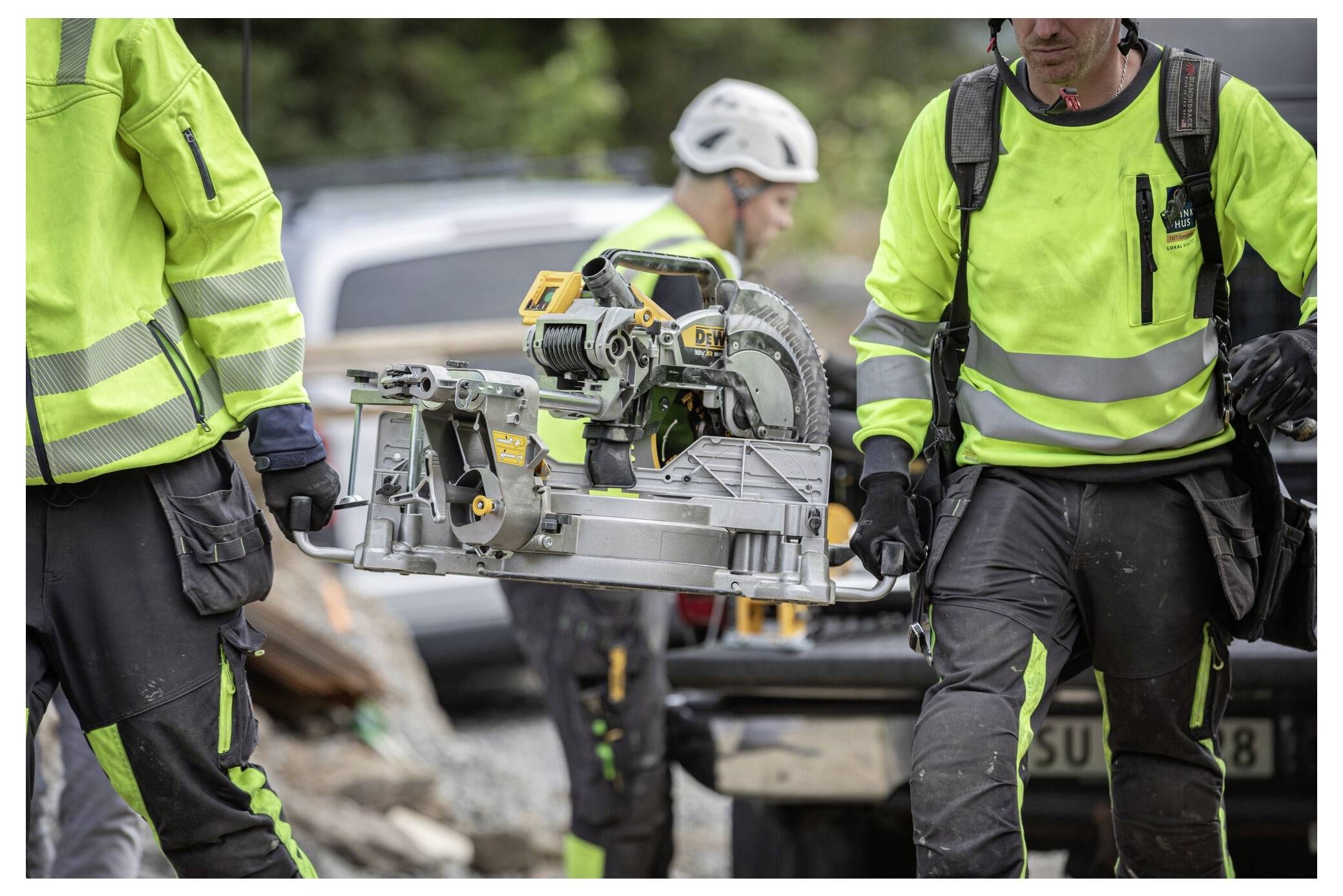 Bauarbeiter in hochsichtbarer Kleidung tragen eine Kreissäge auf einer Baustelle.