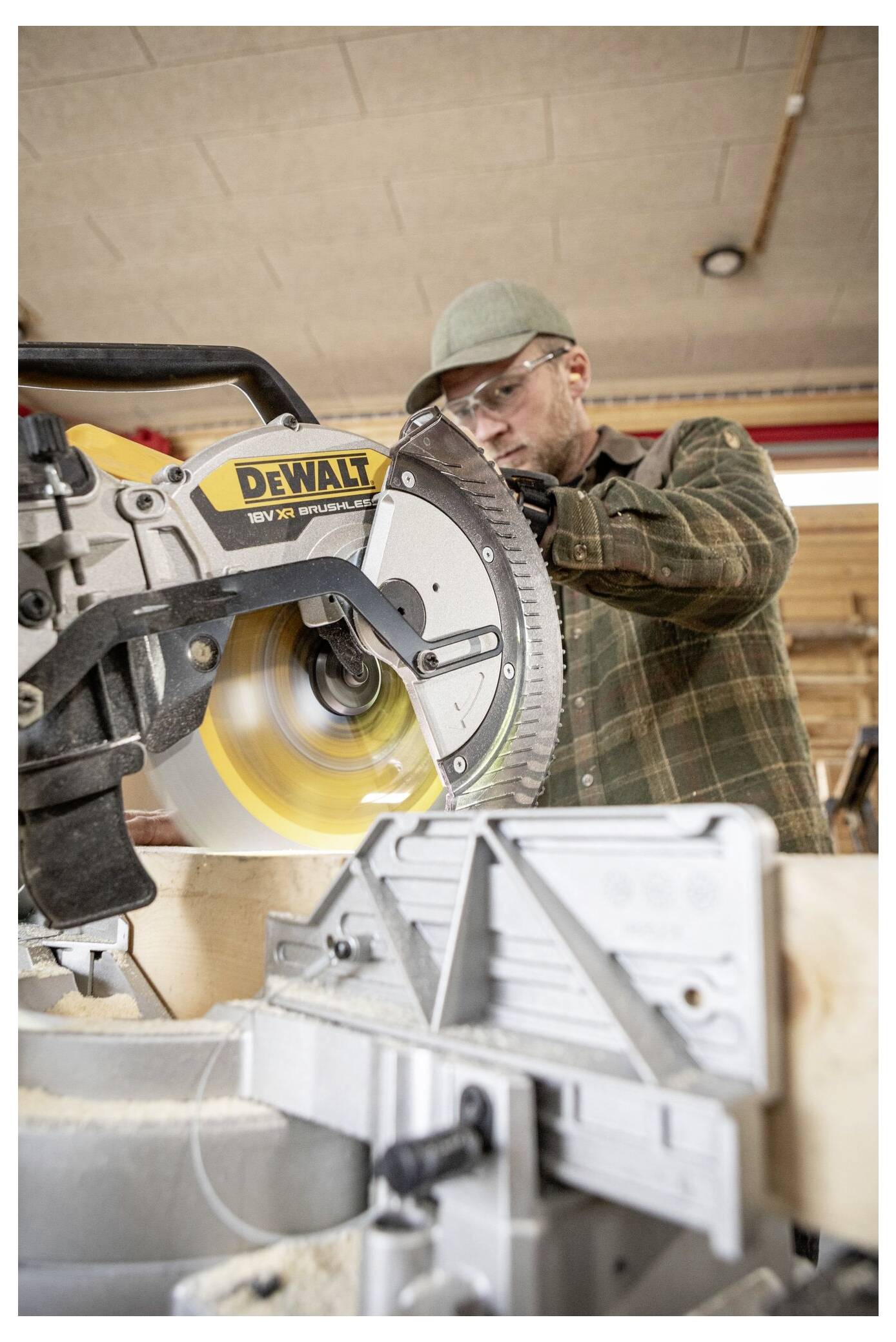 Eine Person in einer Schutzbrille bedient eine Kreissäge in einer Holzwerkstatt und konzentriert sich intensiv darauf, ein Holzstück zu schneiden.