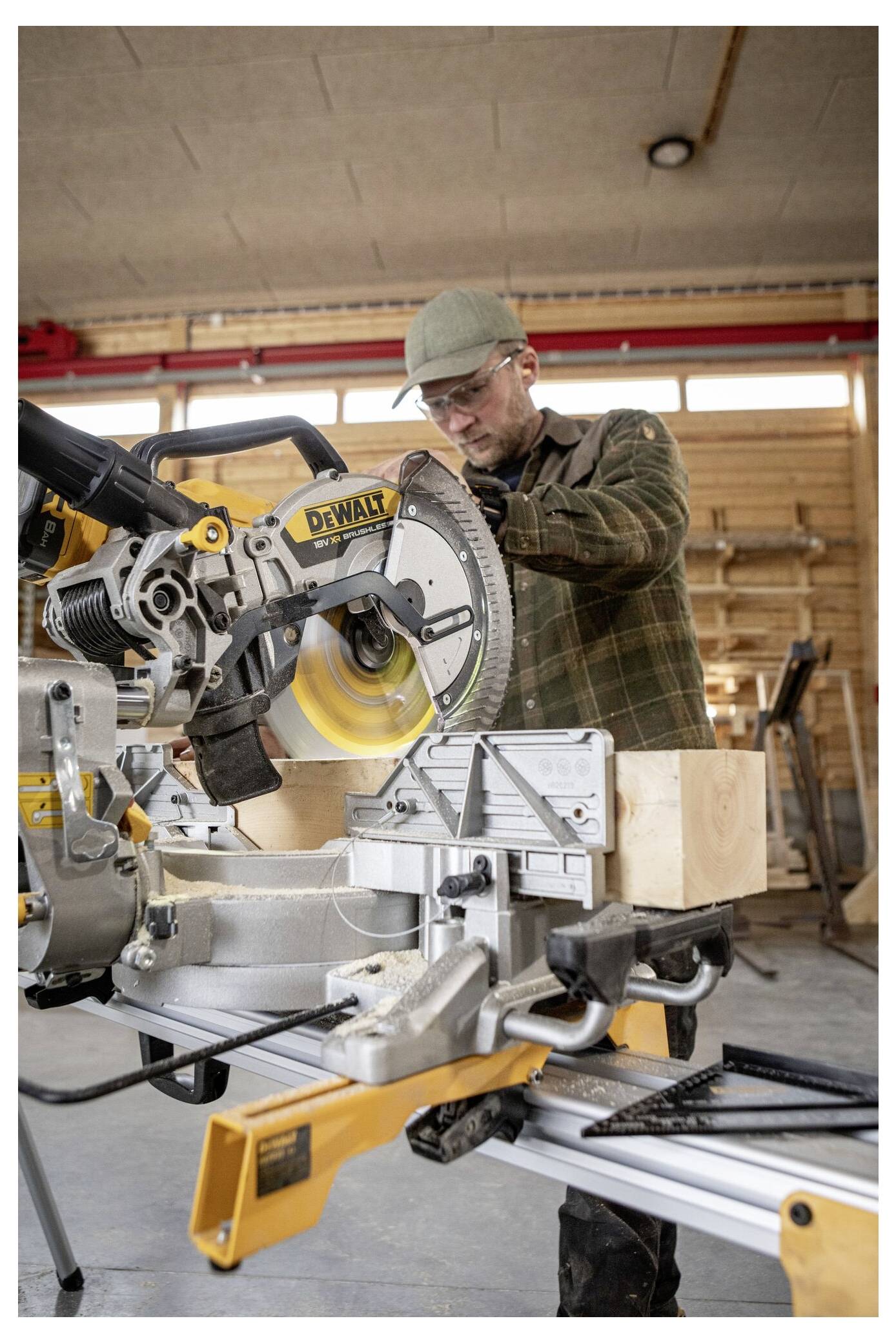 Eine Person, die in einer Werkstatt mit einer Kreissäge Holz schneidet, trägt dabei eine Schutzbrille und eine Mütze.
