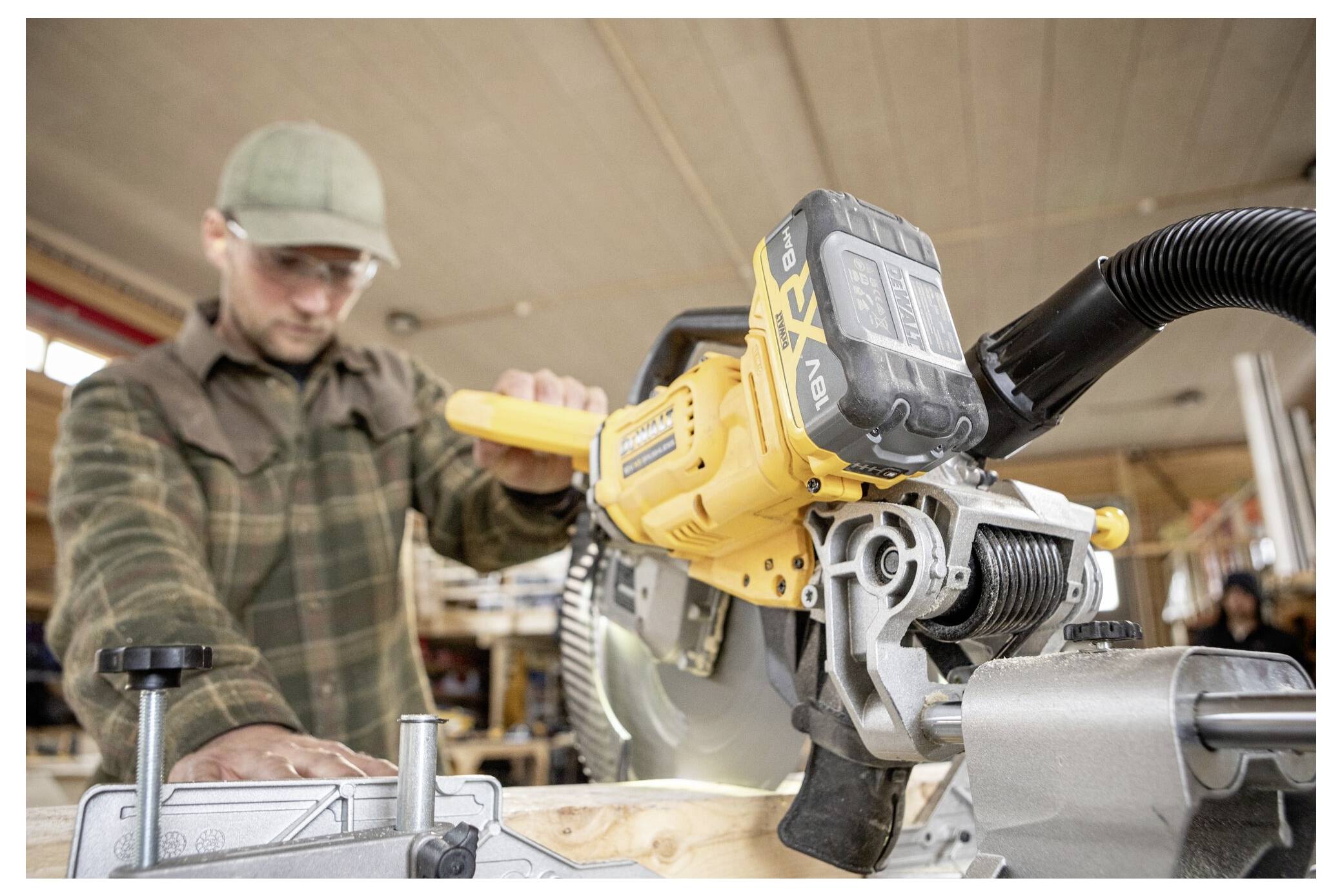 Eine Person in einer Werkstatt bedient eine Kreissäge und schneidet Holz. Der Fokus liegt auf der Säge, die gelb ist und sichtbare Sicherheitsvorrichtungen hat.