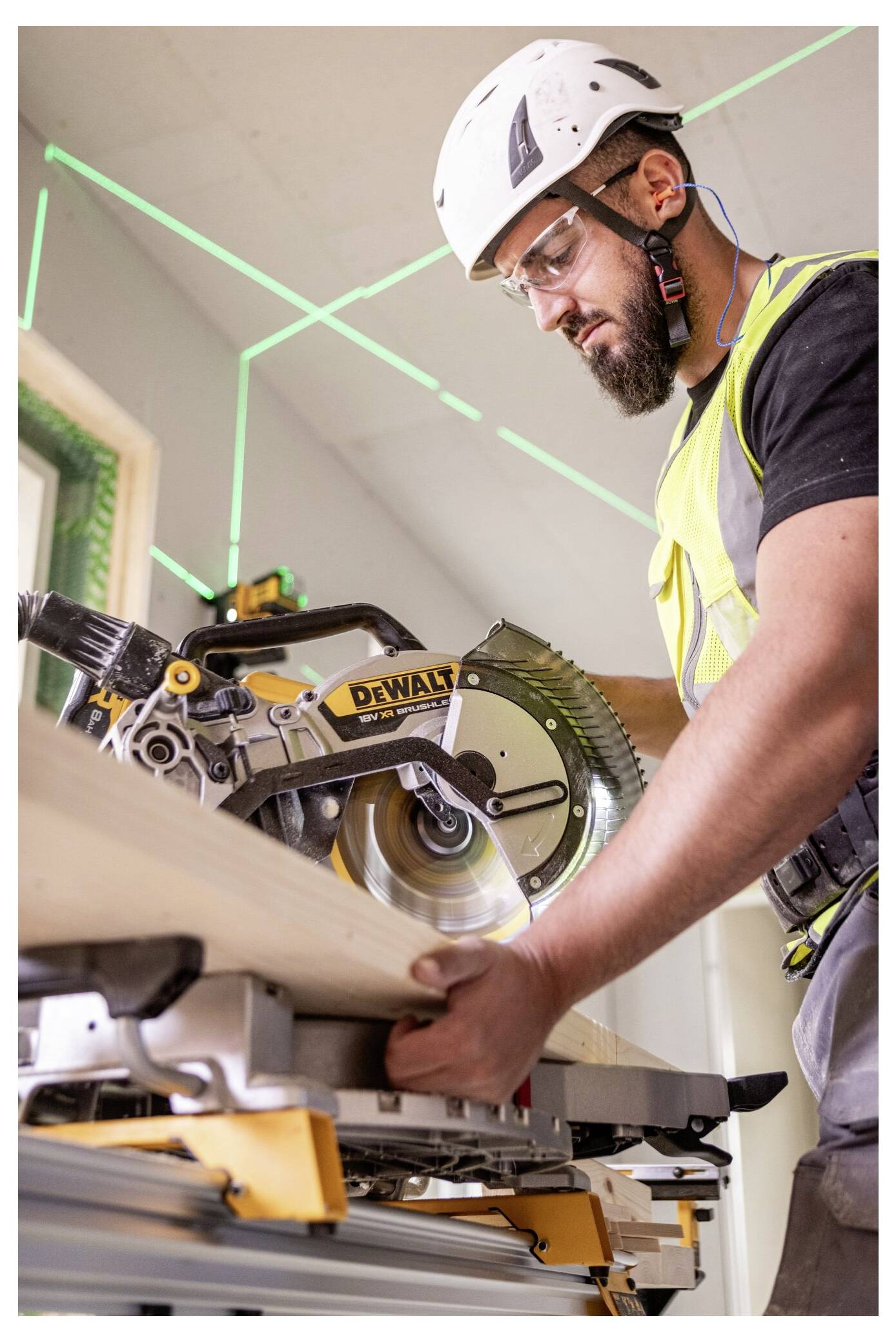 Ein Bauarbeiter mit Helm und Schutzausrüstung bedient eine Kreissäge, um ein Holzbrett auf einer Baustelle zu schneiden.
