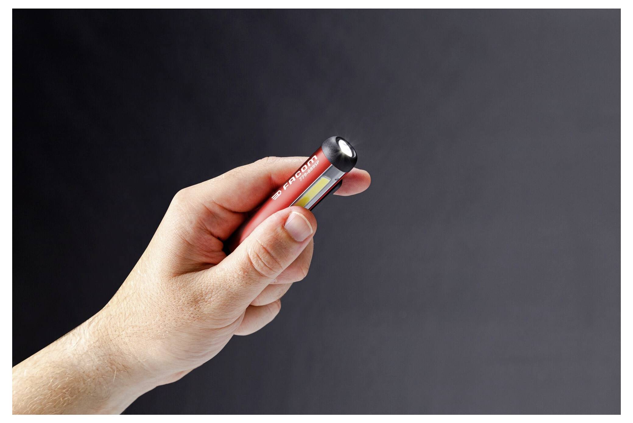 Eine Hand hält eine kleine rote Taschenlampe gegen einen dunklen Hintergrund.