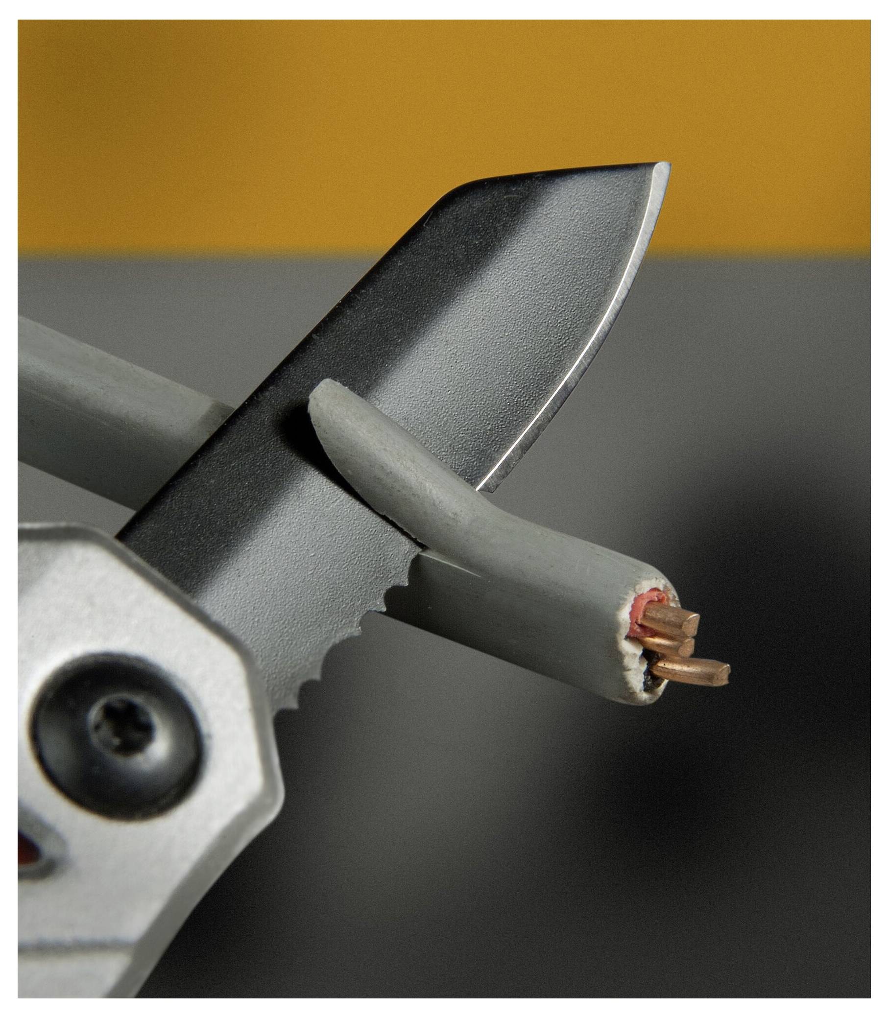 Eine Nahaufnahme von Drahtschneidern, die durch ein graues Stromkabel schneiden, wobei Kupferdrähte freigelegt werden, vor einem unscharfen orange und grauen Hintergrund.