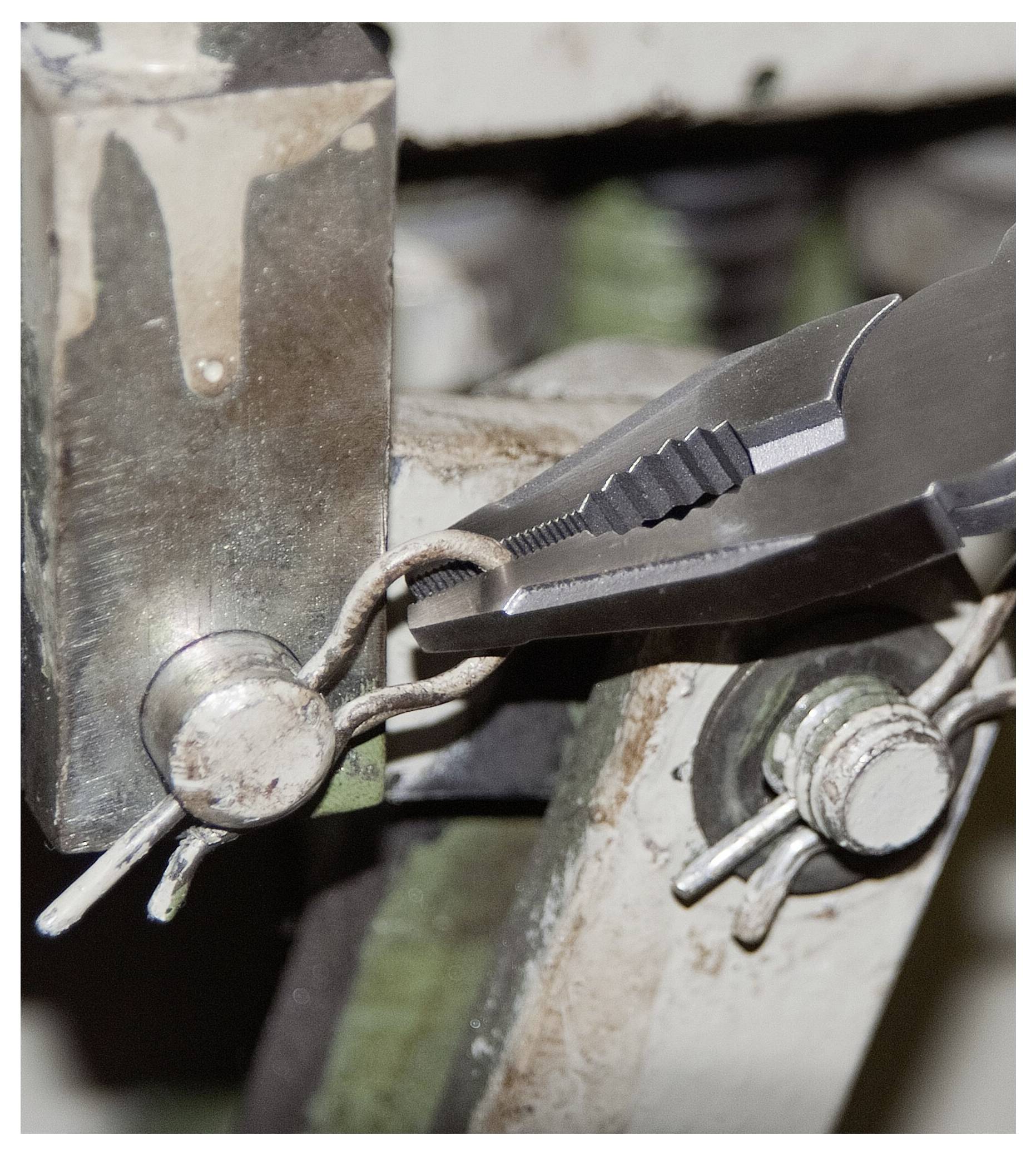 Nahaufnahme einer Zange, die einen Metalldraht an einem Stück Industriemaschine biegt, die eine detaillierte Ansicht des Werkzeuggriffs und der Präzision zeigt.