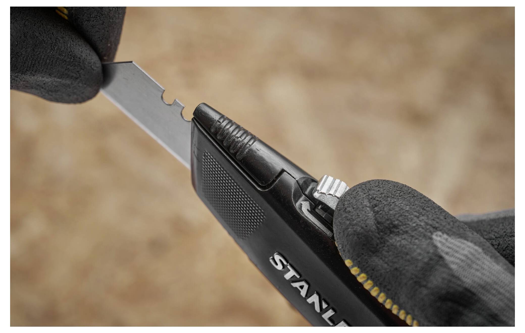 Eine Hand, die einen schwarzen Handschuh trägt, hält ein Universalmesser, während die andere Hand dessen Klinge einstellt oder austauscht und dabei präzises Handling zeigt.