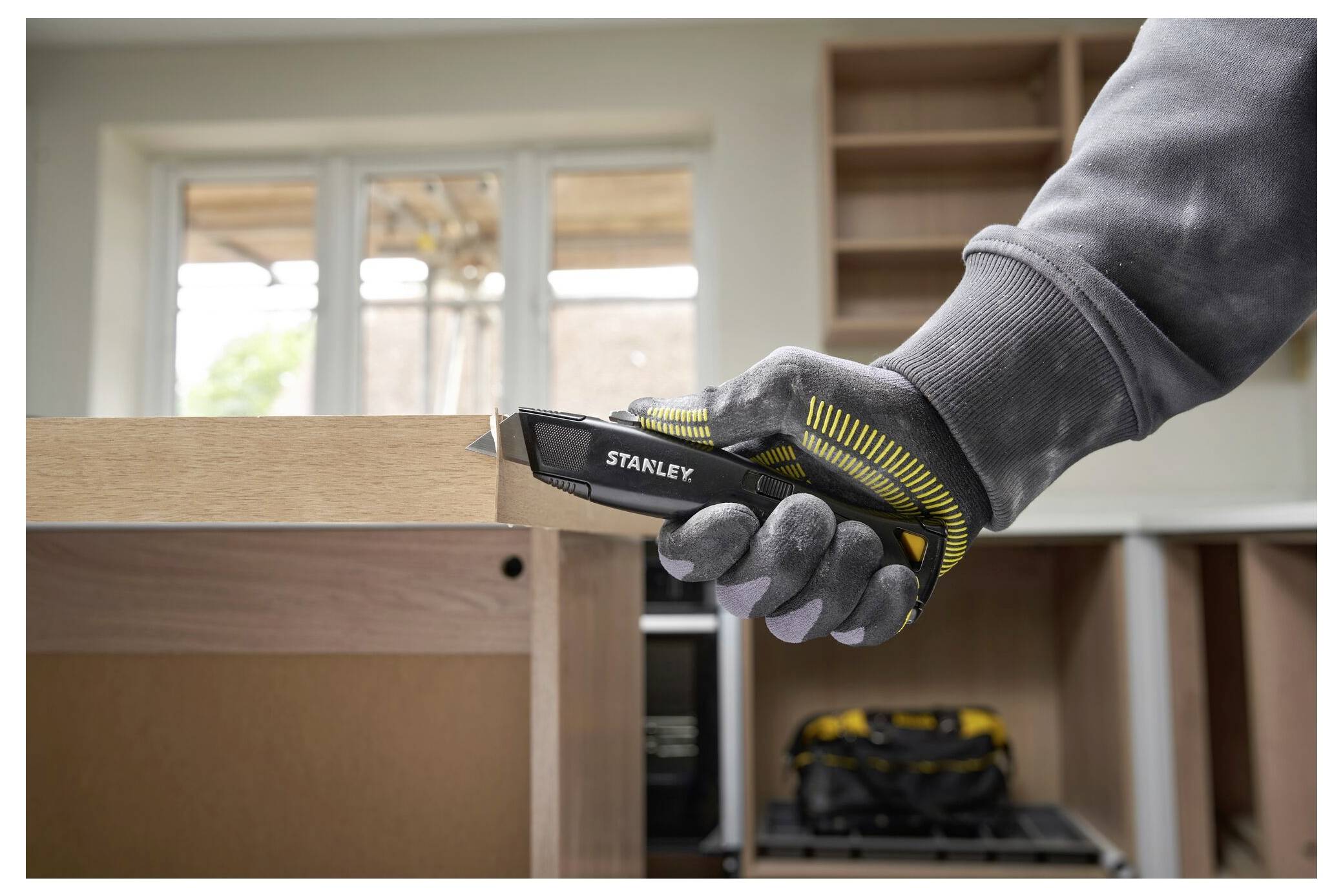 Ein Zimmermann in Schutzausrüstung bedient eine Kreissäge, um einen Holzbalken in einer Werkstatt zu schneiden, die mit Holzmaterialien gefüllt ist.