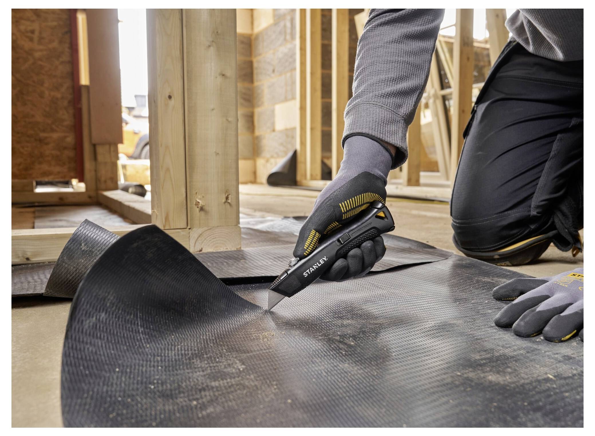 Eine Nahaufnahme einer Gehrungssäge in einer Werkstatt, mit einer angeschlossenen Absauganlage zur Staubabsaugung. Holzstapel sind im Hintergrund zu sehen.