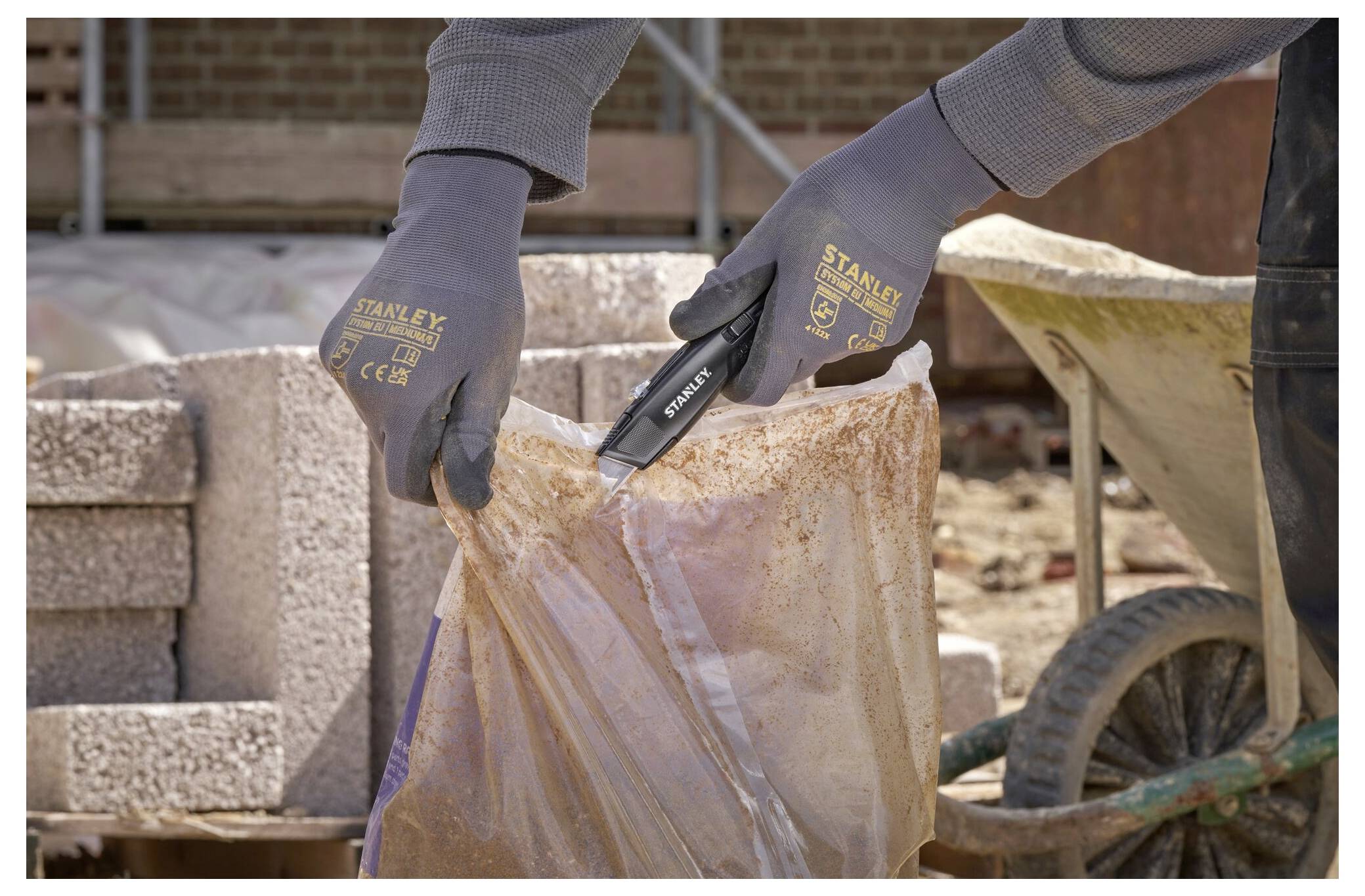 Eine Person mit Handschuhen führt eine Rasierklinge in ein Universalmesser ein. Das Messer ist teilweise auf einer Holzoberfläche zerlegt.