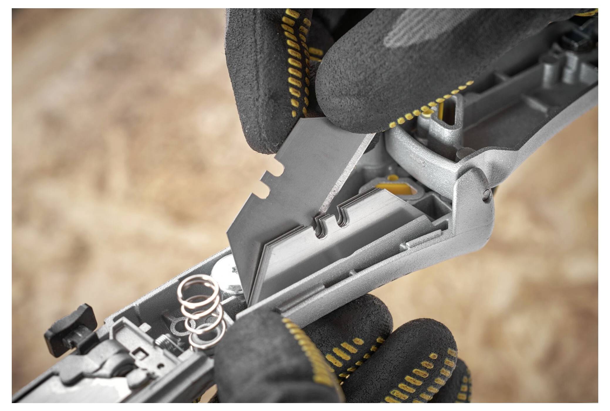 Behandschuhte Hände ersetzen eine Rasierklingenklinge in einem Schneidewerkzeug, wobei ordnungsgemäße Handhabung und Sicherheitsvorkehrungen zur Wartung gezeigt werden.