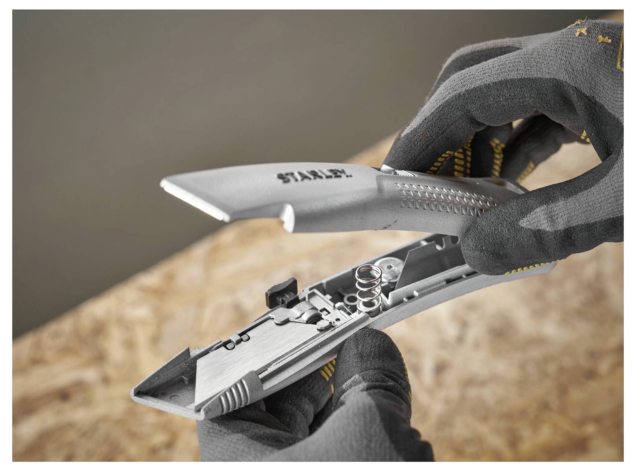 Eine Person, die Handschuhe trägt, zerlegt ein Cuttermesser und enthüllt dabei seine internen Komponenten, einschließlich Federn und eines Klingenlagerungskompartiments.