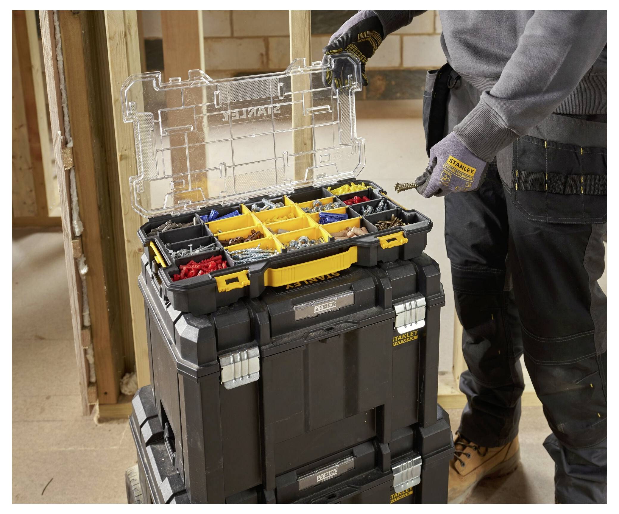 Eine Person organisiert verschiedene Schrauben und Bolzen in einer tragbaren Kunststoff-Aufbewahrungsbox mit mehreren Fächern. Der offene Deckel zeigt den Inhalt.