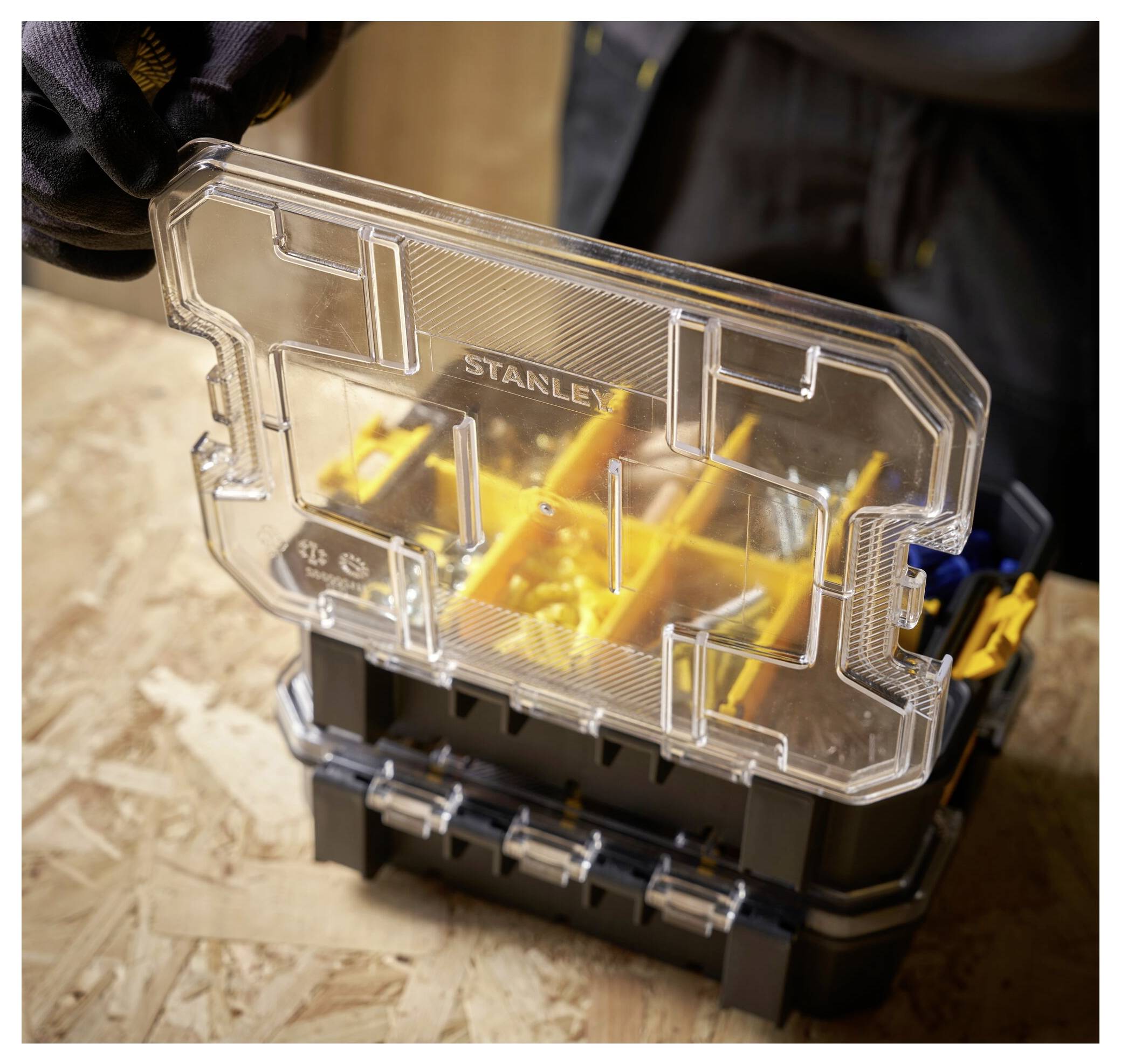 Eine Person mit Handschuhen benutzt ein Elektrowerkzeug in einer Außenumgebung. Das Werkzeug ist ein gelb-schwarzer Bohrer mit Fokus auf den Batteriewechsel.