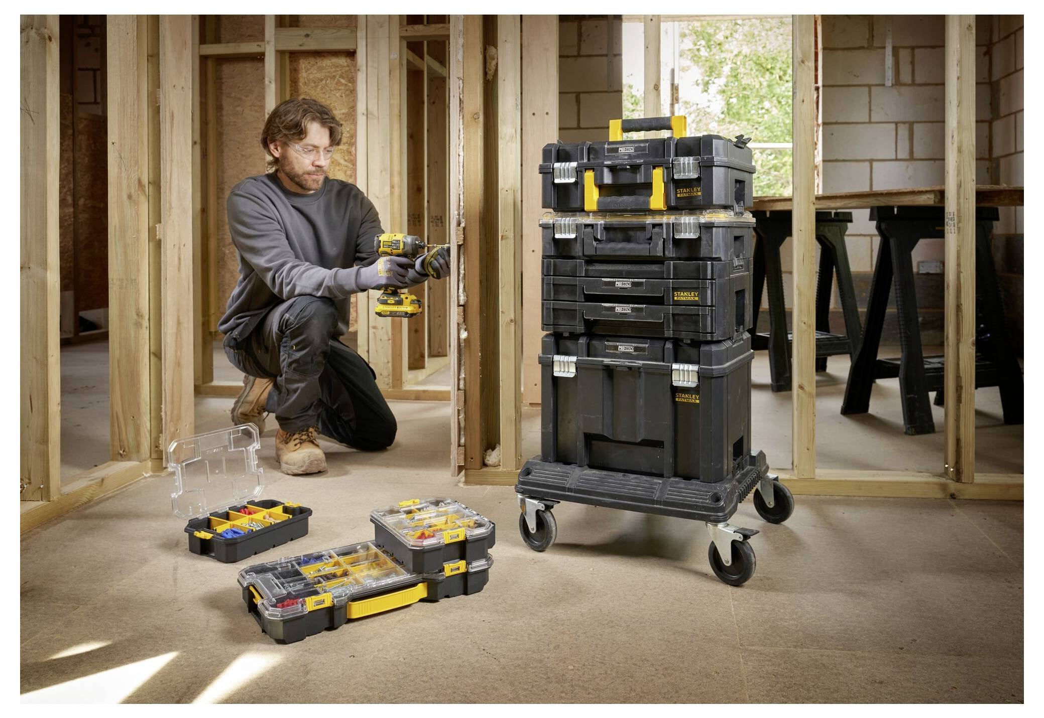 Eine Person mit Handschuhen öffnet einen gelben Verschluss an einer schwarzen Lagerkiste, die mit kleinen roten Gegenständen gefüllt ist und eine Organisierung oder Reparatur andeutet.