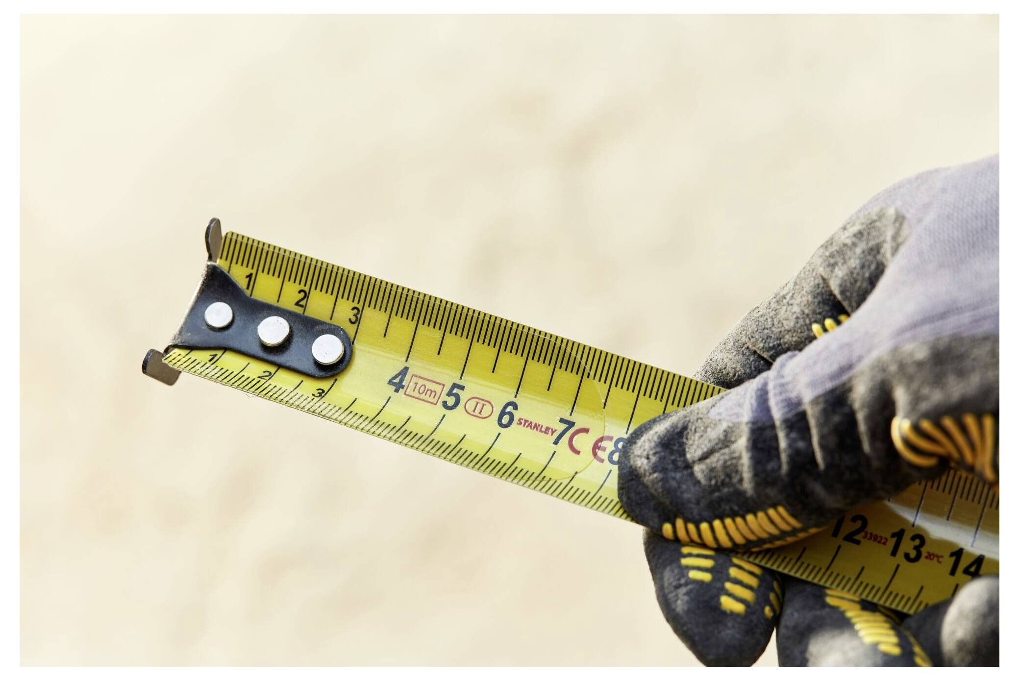 Eine Person benutzt einen gelben tragbaren Bläser, um Staub von einem Bauplatzenboden zu entfernen, umgeben von Holzrahmen und Sperrholzwänden.