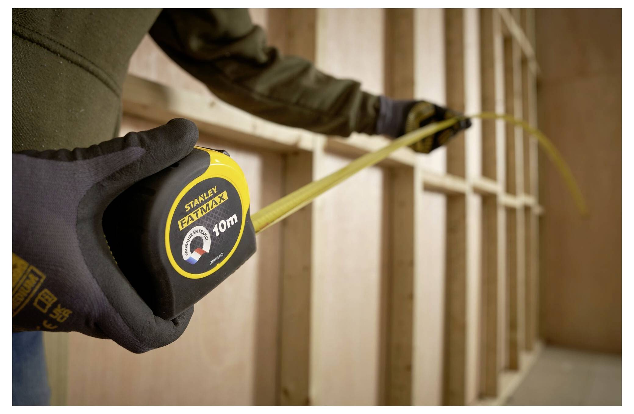 Eine Person, die Arbeitshandschuhe trägt, hält ein Stahlmaßstab ausgestreckt, wobei die Zahlen sichtbar sind, vor einem unscharfen Hintergrund.