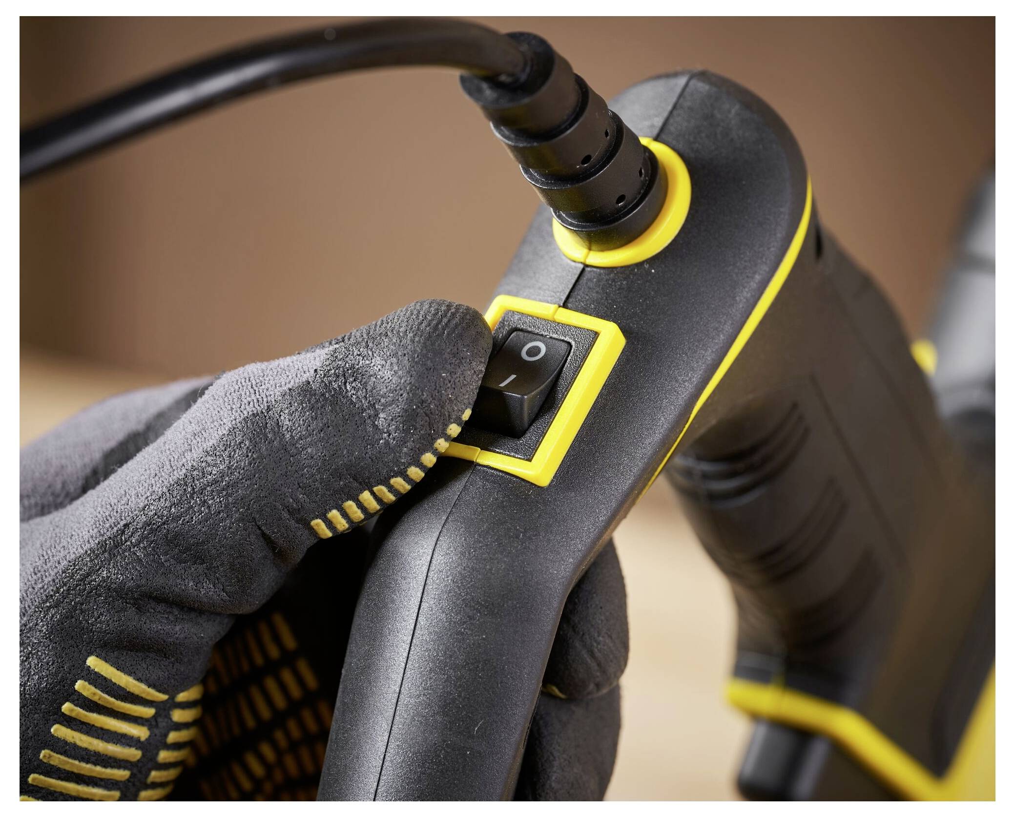 Eine handschuhtragende Hand betätigt den Stromschalter an einem schwarzgelben Elektrowerkzeug, möglicherweise um es zu aktivieren oder deaktivieren.