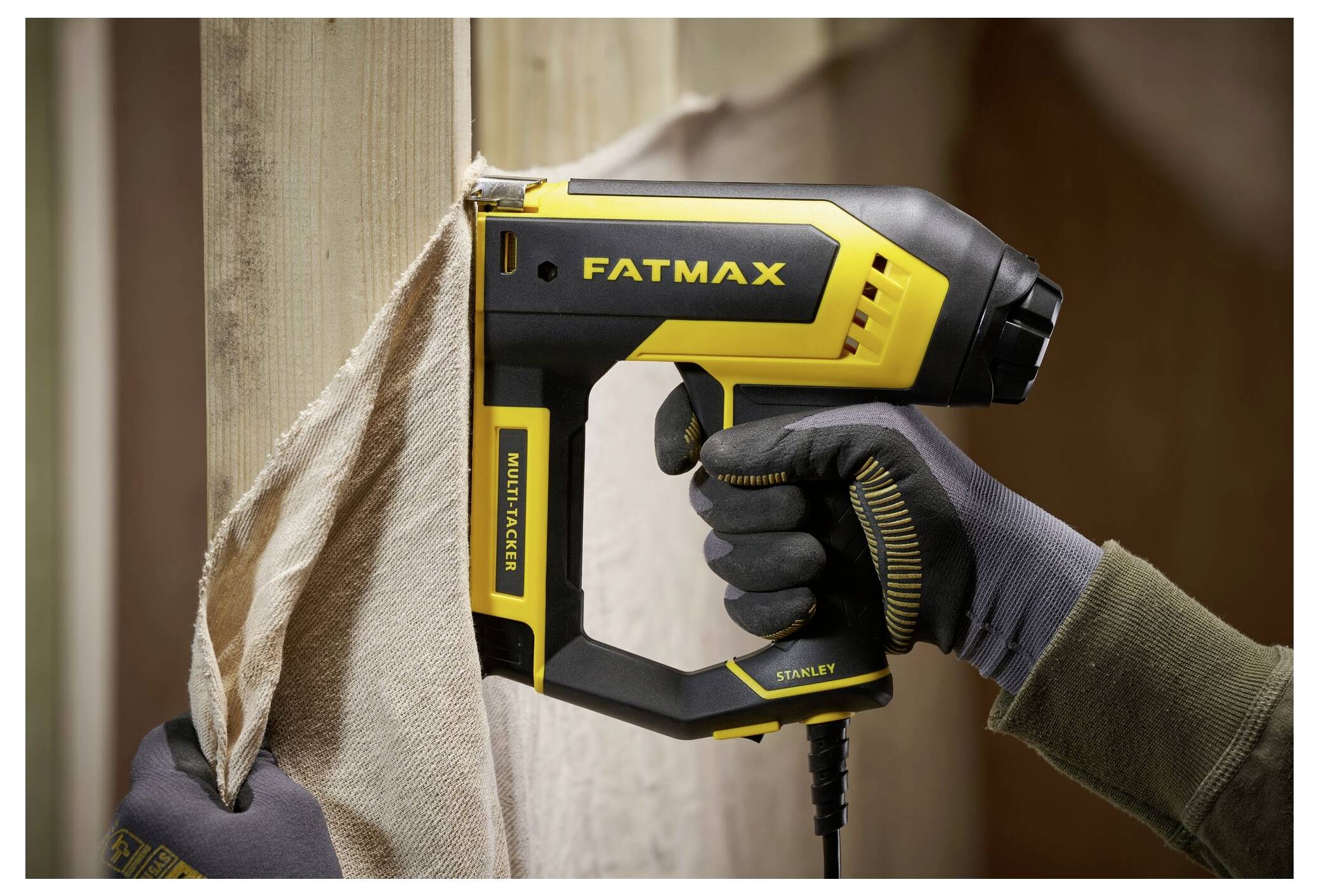 Eine Person in Arbeitshandschuhen hält ein gelbes 5m Stahllineal, das entlang eines Holzrahmens ausgestreckt ist und präzise Messaktiviät anzeigt.