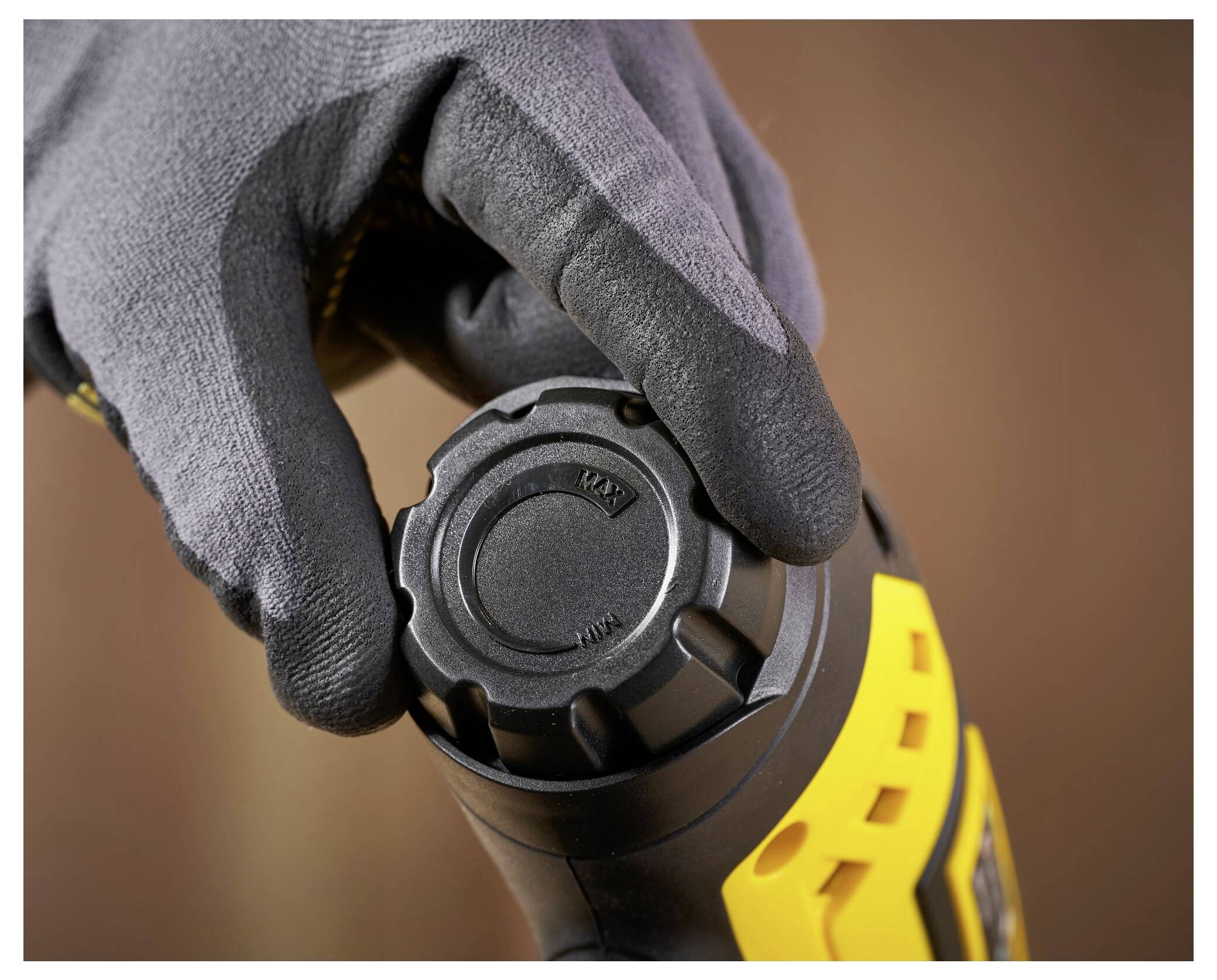 Eine Person, die eine Schutzbrille und Handschuhe trägt, benutzt einen gelben Stanley-Elektrobohrer, um ein Loch in ein Holzbrett zu bohren und dabei Holzspäne zu erzeugen.