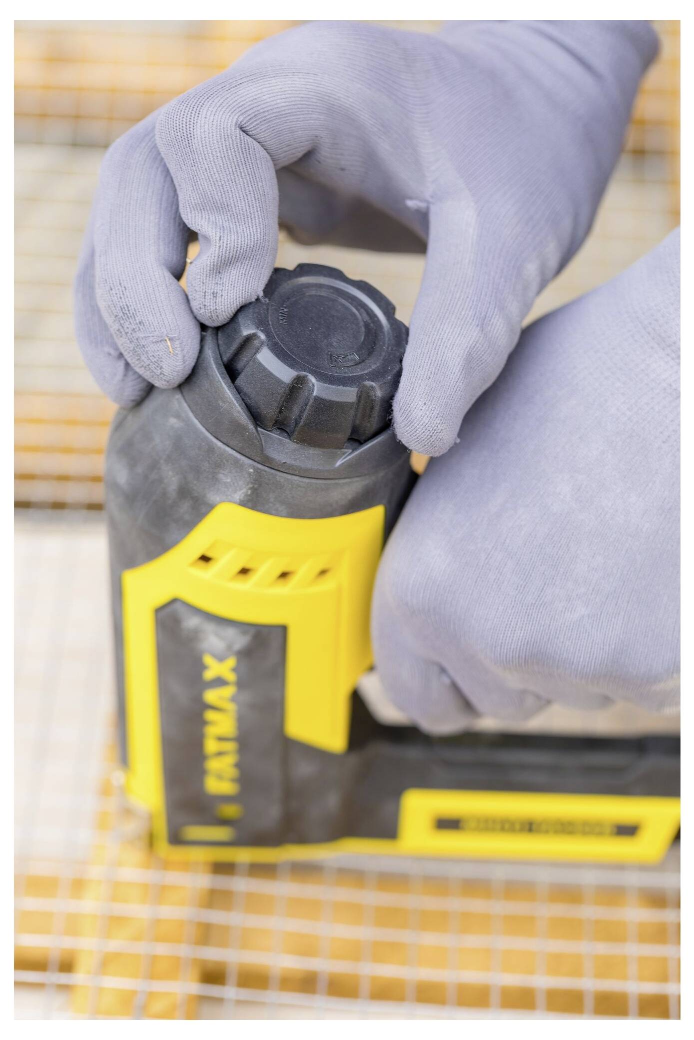 Eine Person mit grauen Handschuhen benutzt eine gelbe Tacker auf orange-weißem Netzstoff.