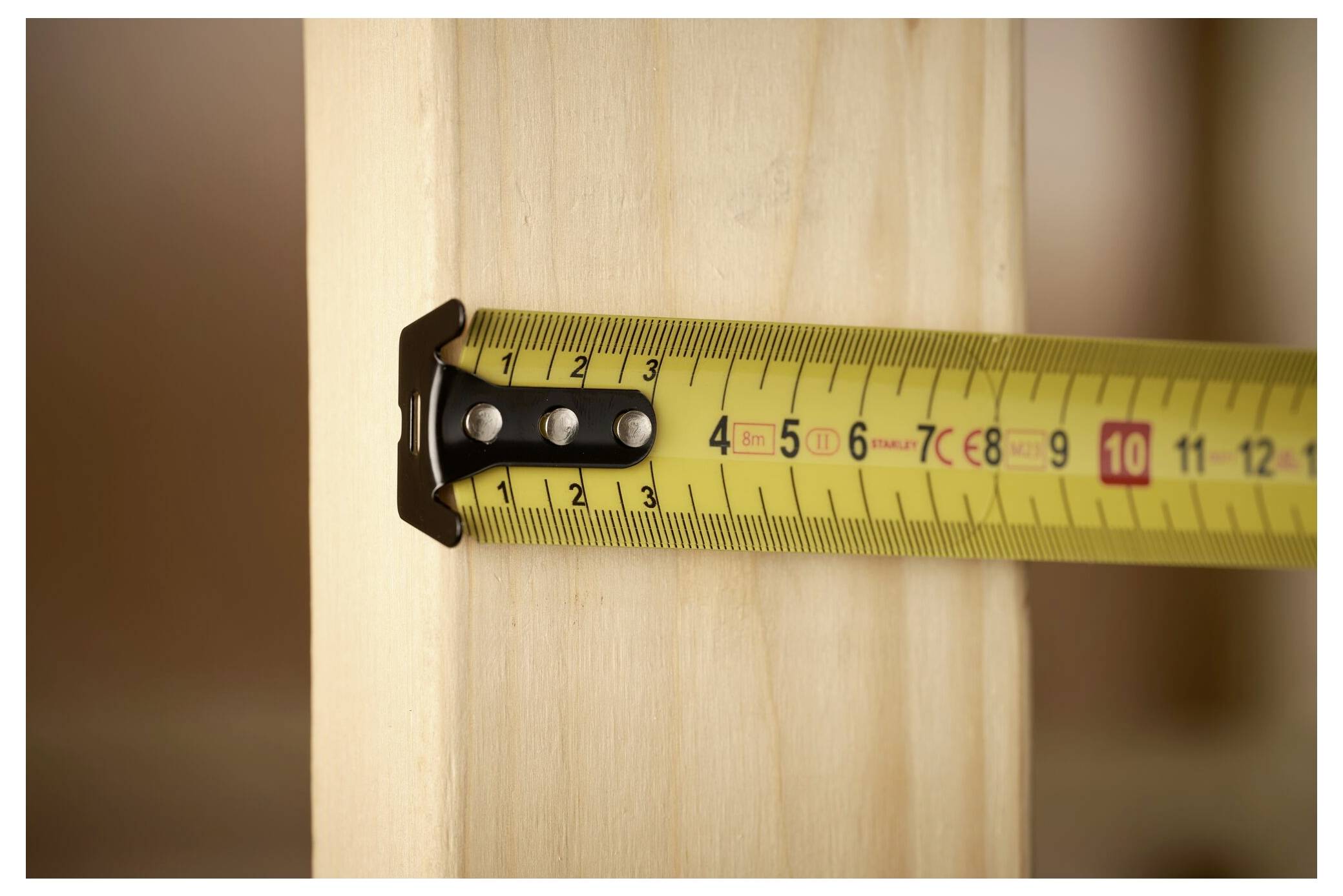 Ein gelbes Messstab wird über einen Holzbalken gezogen und zeigt eine Messung von 11 Zentimetern.