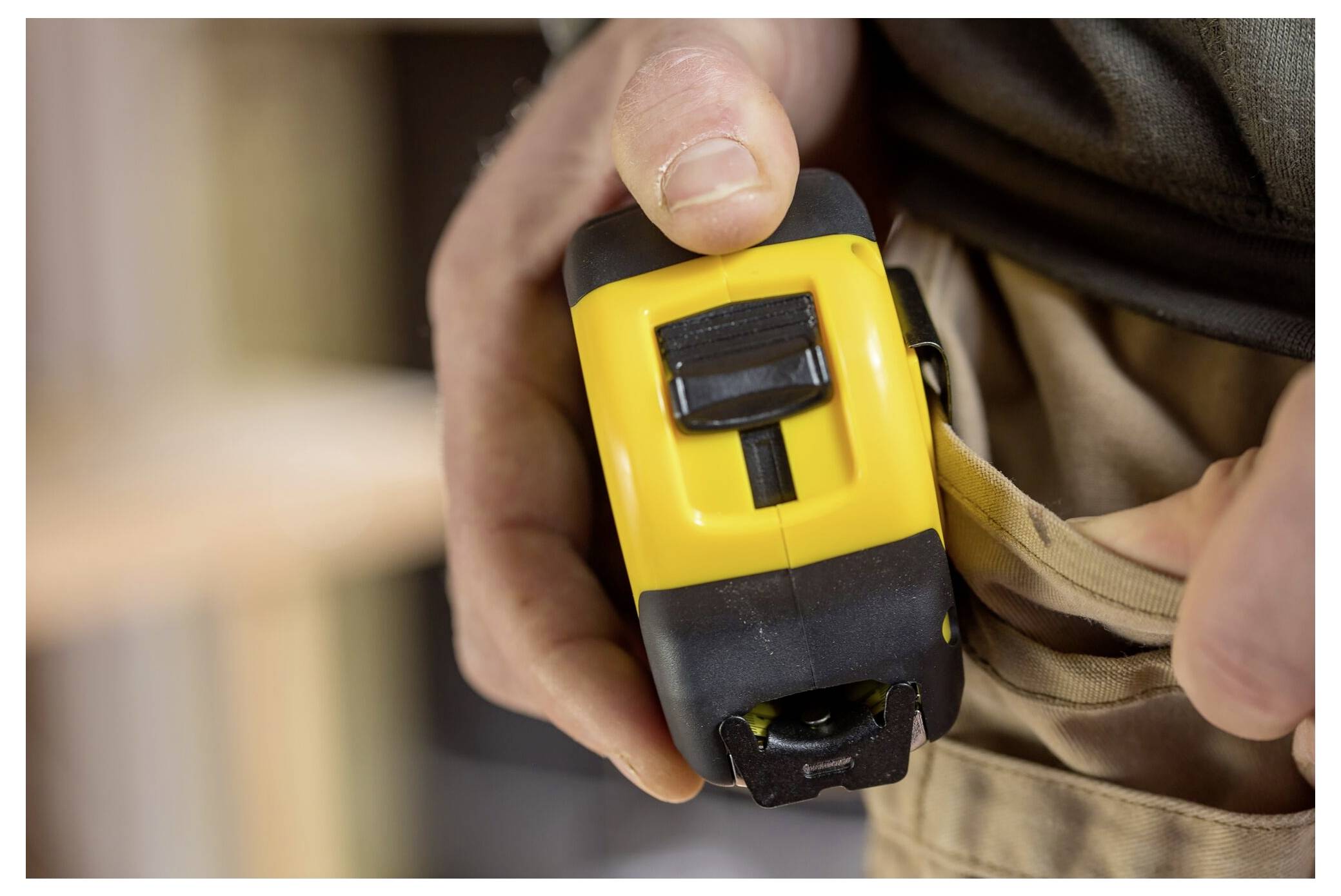 Eine Person hält ein gelb-schwarzes Stahllineal und befestigt es an einem Werkzeuggürtel.