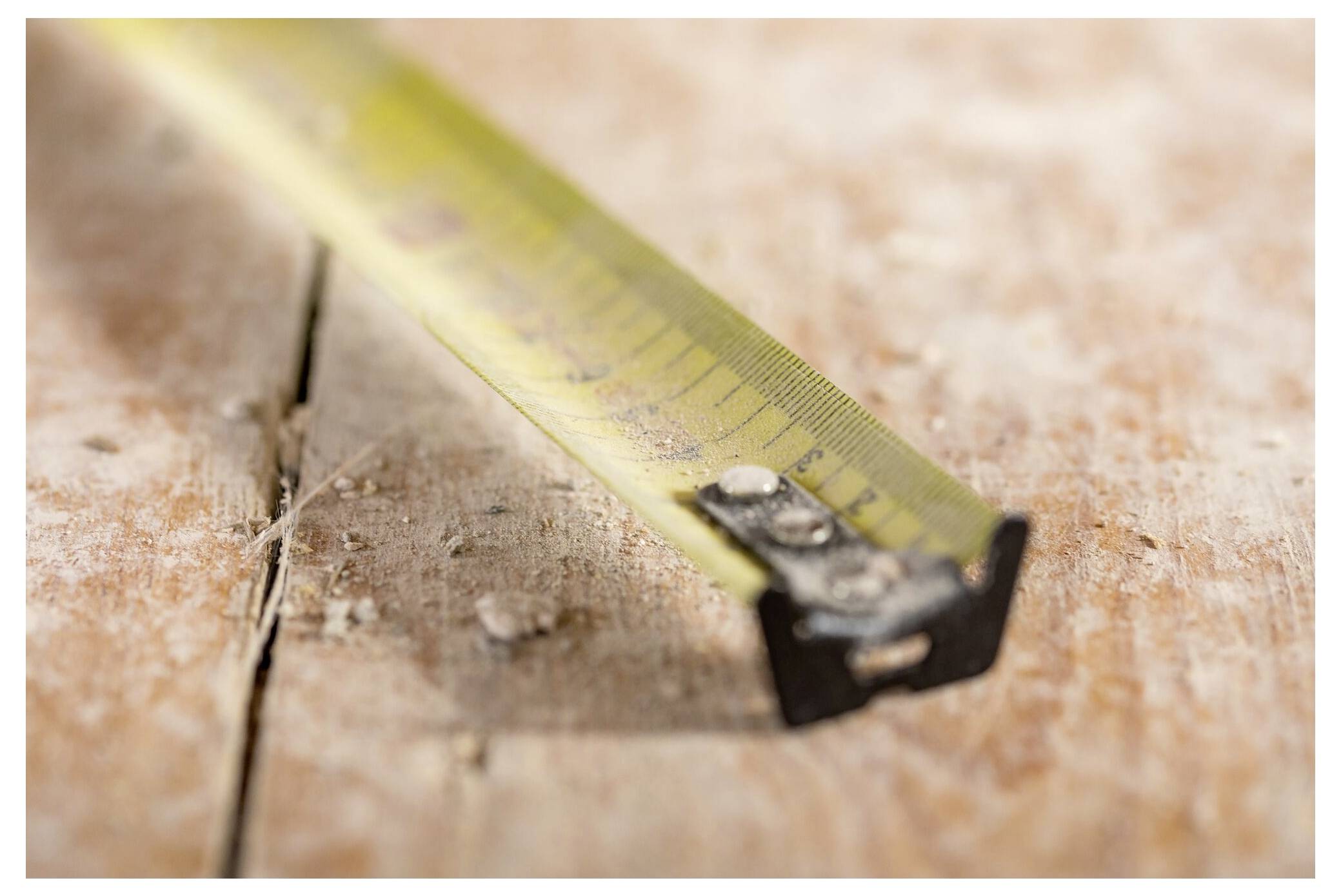 Eine Nahaufnahme eines staubigen Messbands, das auf einer Holzoberfläche ausgestreckt ist und auf ein laufendes Bau- oder Tischlerprojekt hindeutet.