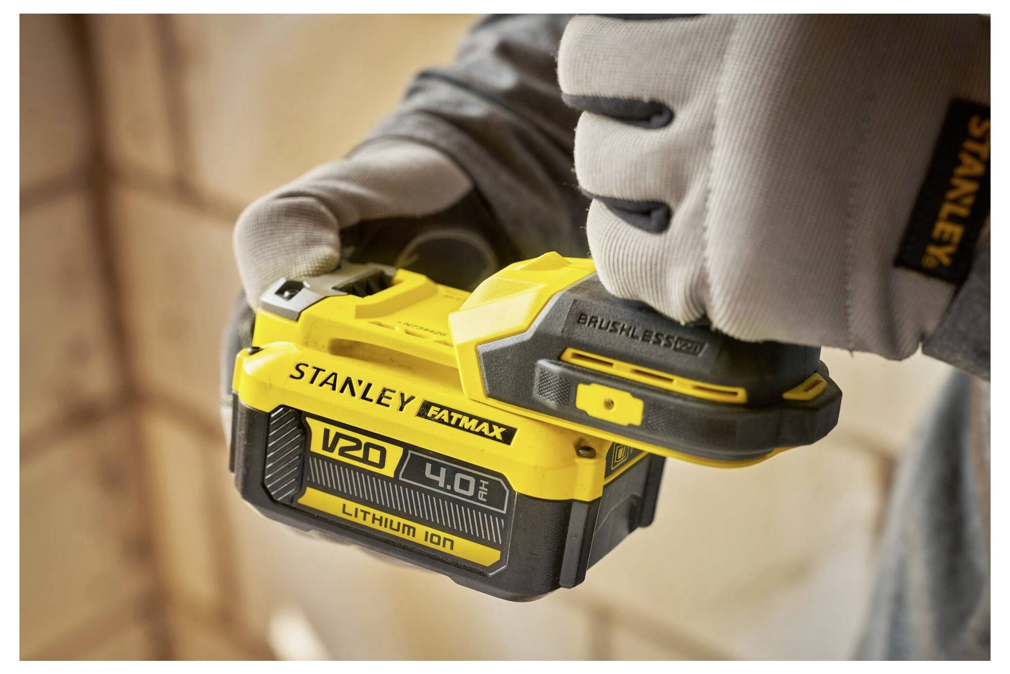 Eine Person mit Handschuhen hält eine Stanley Fatmax V20 4,0 Ah Lithium-Ionen-Batterie, mit Fokus auf die Branding und das Design des Geräts.