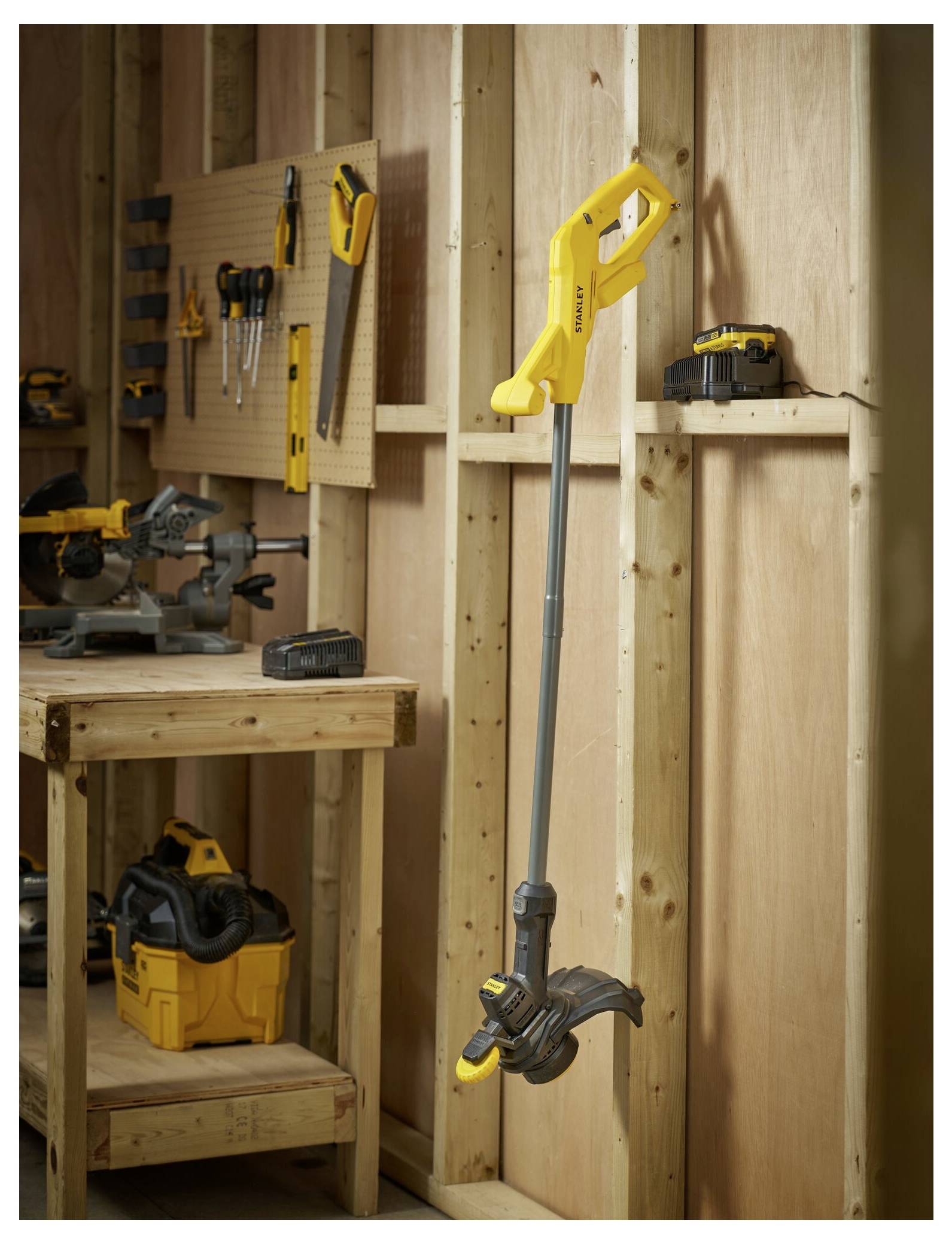 Ein gelber Gartenfräser hängt an einer Holzwand in einer Werkstatt, umgeben von verschiedenen Werkzeugen und Ausrüstungen auf der Werkbank und den Regalen.