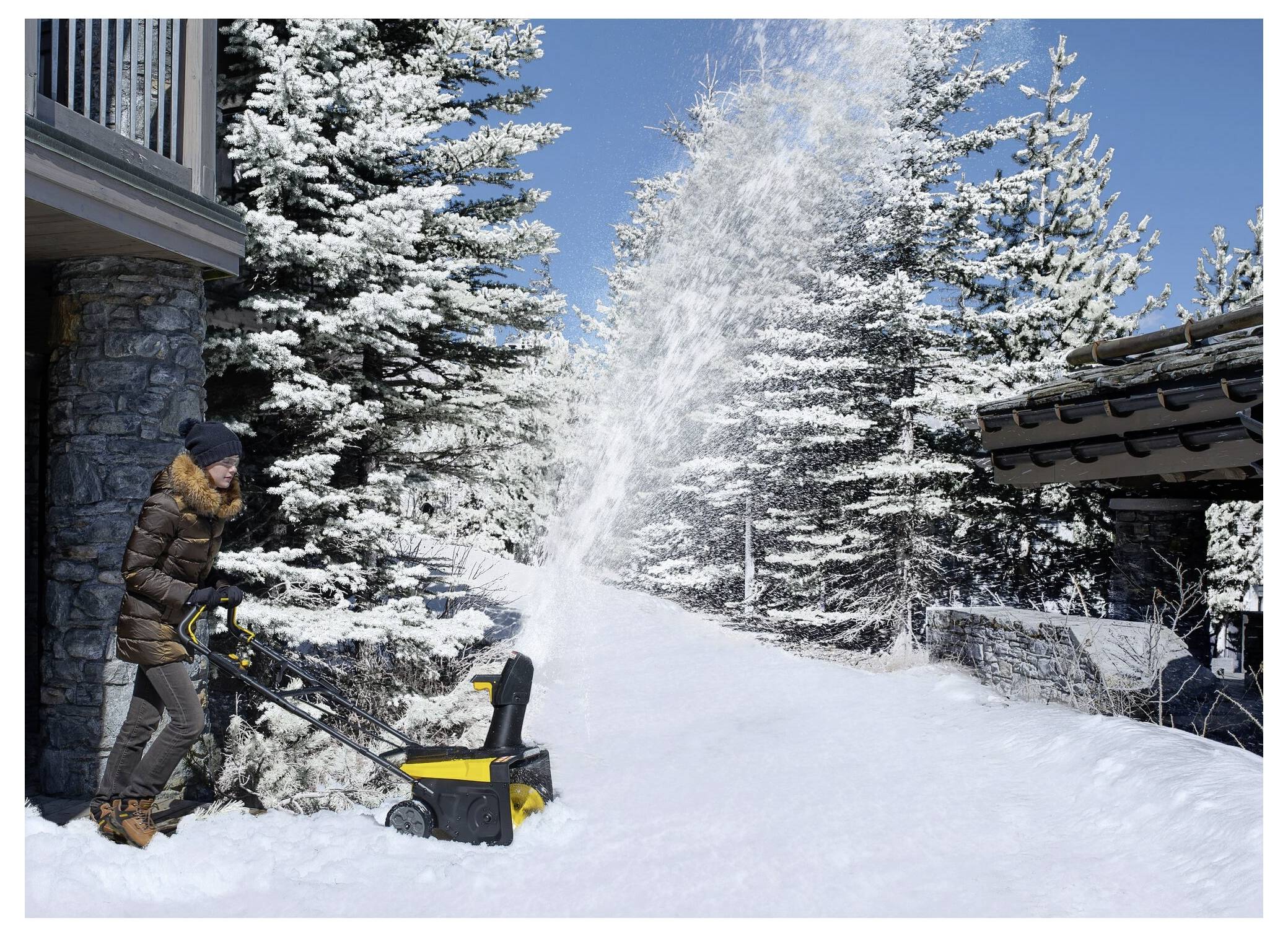 Eine Person bedient einen Schneefräser und räumt einen Weg in einem verschneiten Waldgebiet, während schneebeladene Bäume unter einem klaren blauen Himmel stehen.