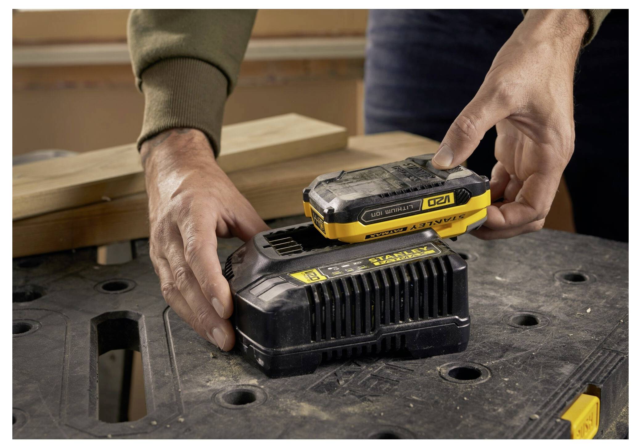 Eine Person mit Handschuhen verwendet eine gelb-schwarze Stanley Fatmax Nagelschussmaschine, um eine Fußleiste an Trockenbauwand zu befestigen, wobei sich Holzspäne auf dem Boden befinden.