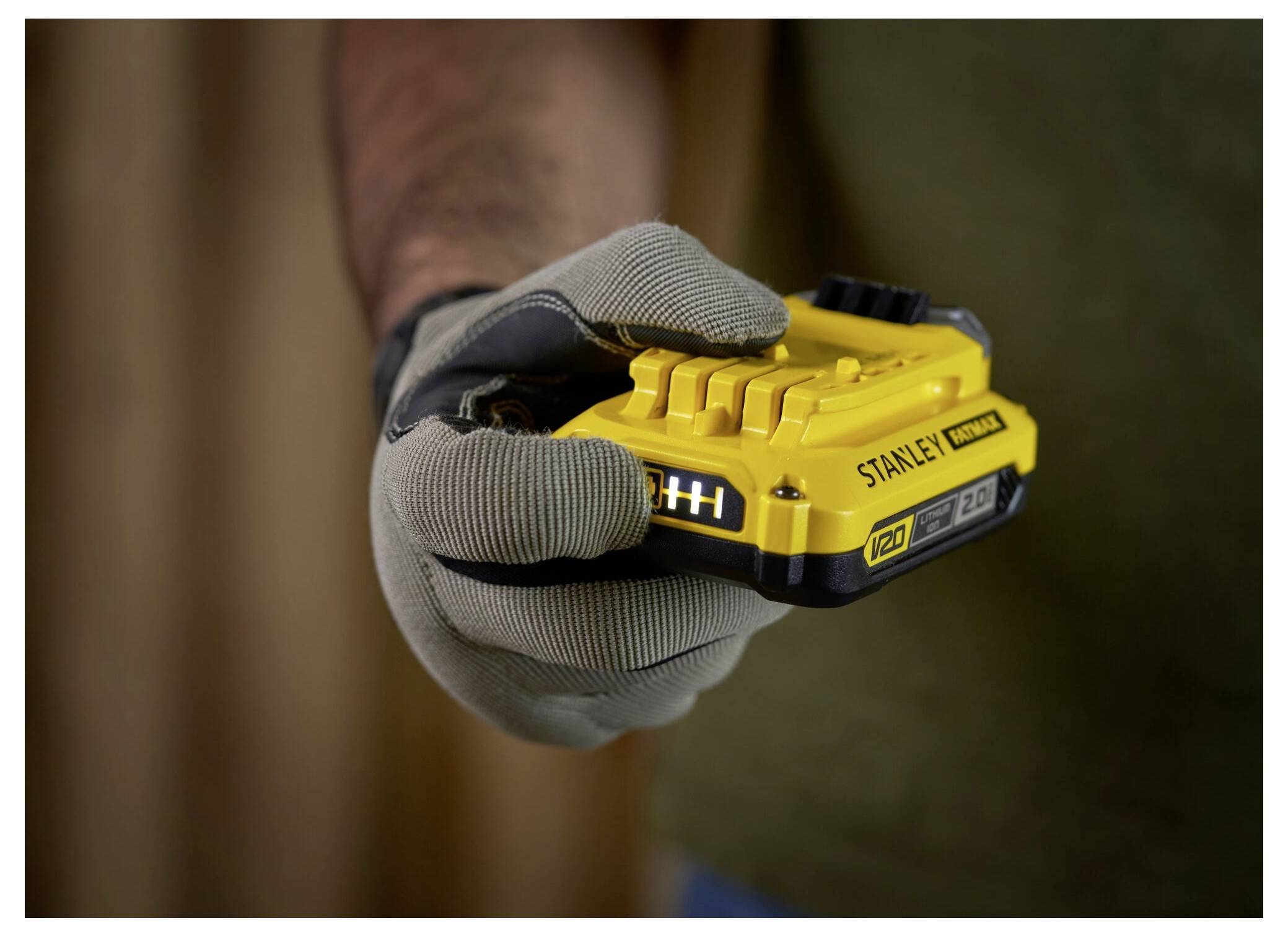 Hände halten einen gelben kabellosen Elektroschrauber gegen eine graue Backsteinmauer und zeigen dabei seinen 20-V-Lithium-Ionen-Akku.