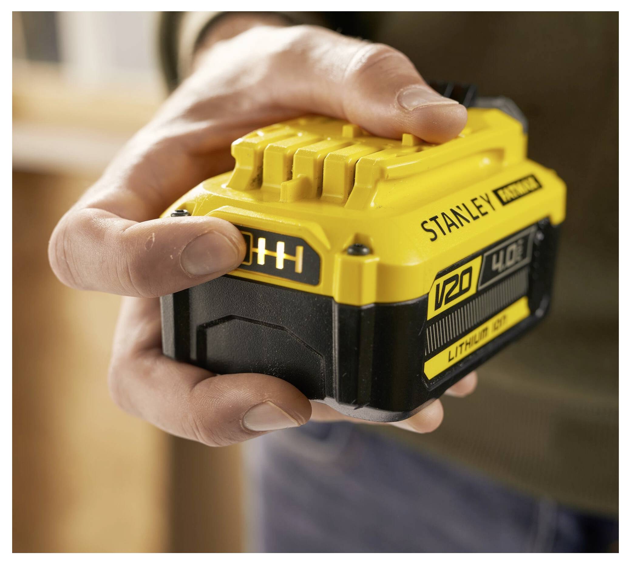 Eine Person hält einen gelben Stanley V20 Lithium-Ionen-Akku mit 4,0 Ah, was zeigt, dass dieser Teil eines Elektrowerkzeugsystems ist.