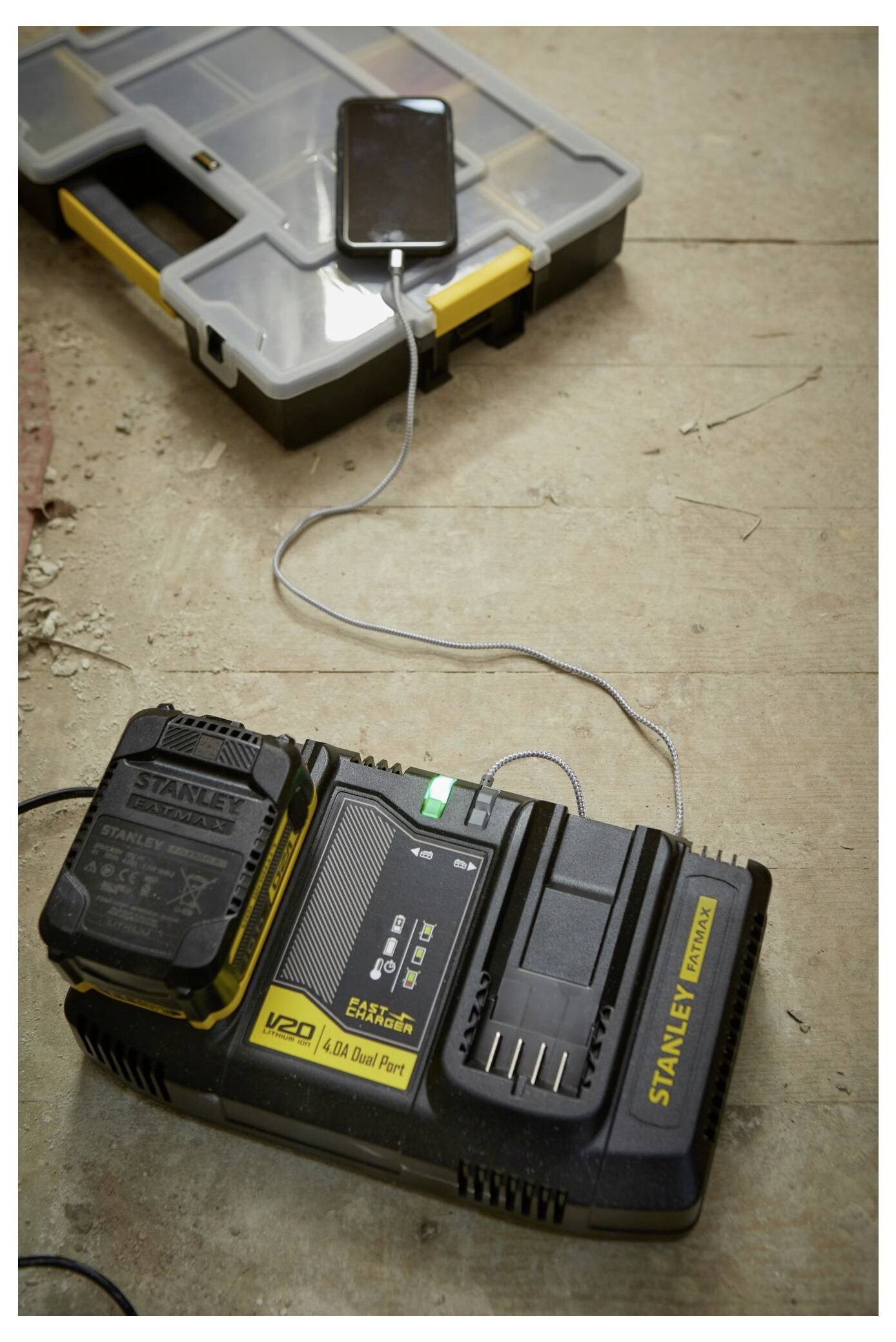 Eine gelb-schwarze Elektrowerkzeug-Batterie auf einem Ladegerät, auf einem Werkstatttisch mit Holzbrettern im Hintergrund platziert.