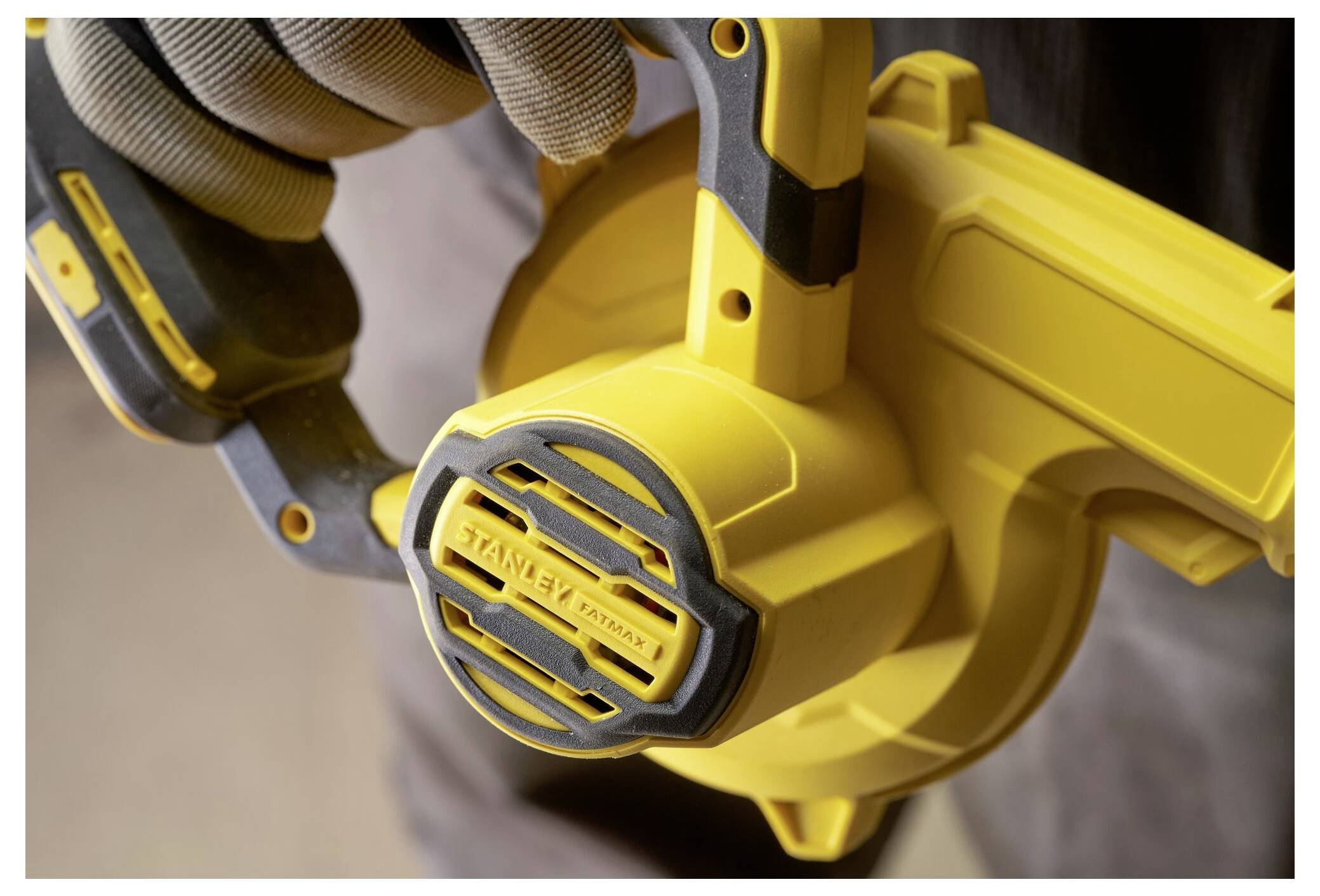 Eine Person, die einen Handschuh trägt, hält ein gelbes tragbares Blaswerkzeug und konzentriert sich auf das Markenetikett in der Mitte der kreisförmigen Öffnung des Werkzeugs.